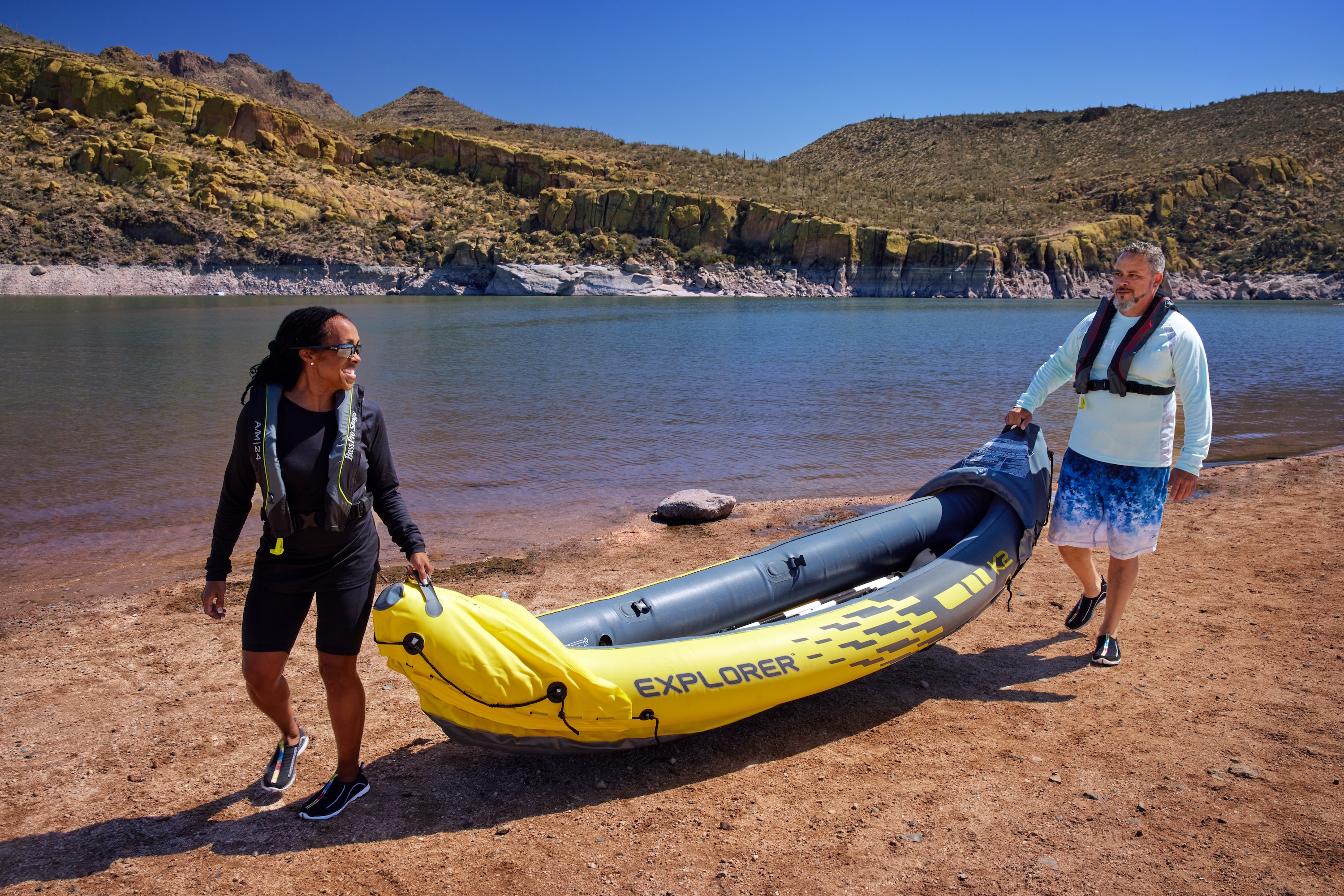 Robin and Warren hold an inflatable kayak by a lake. 