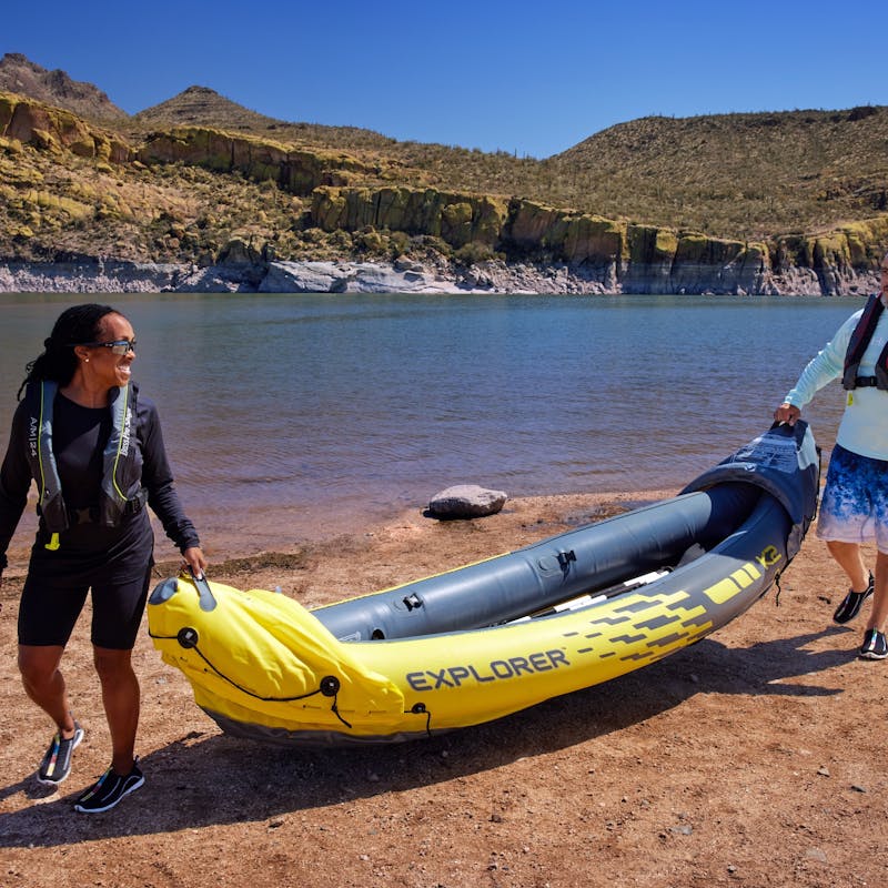 Robin and Warren hold an inflatable kayak by a lake.
