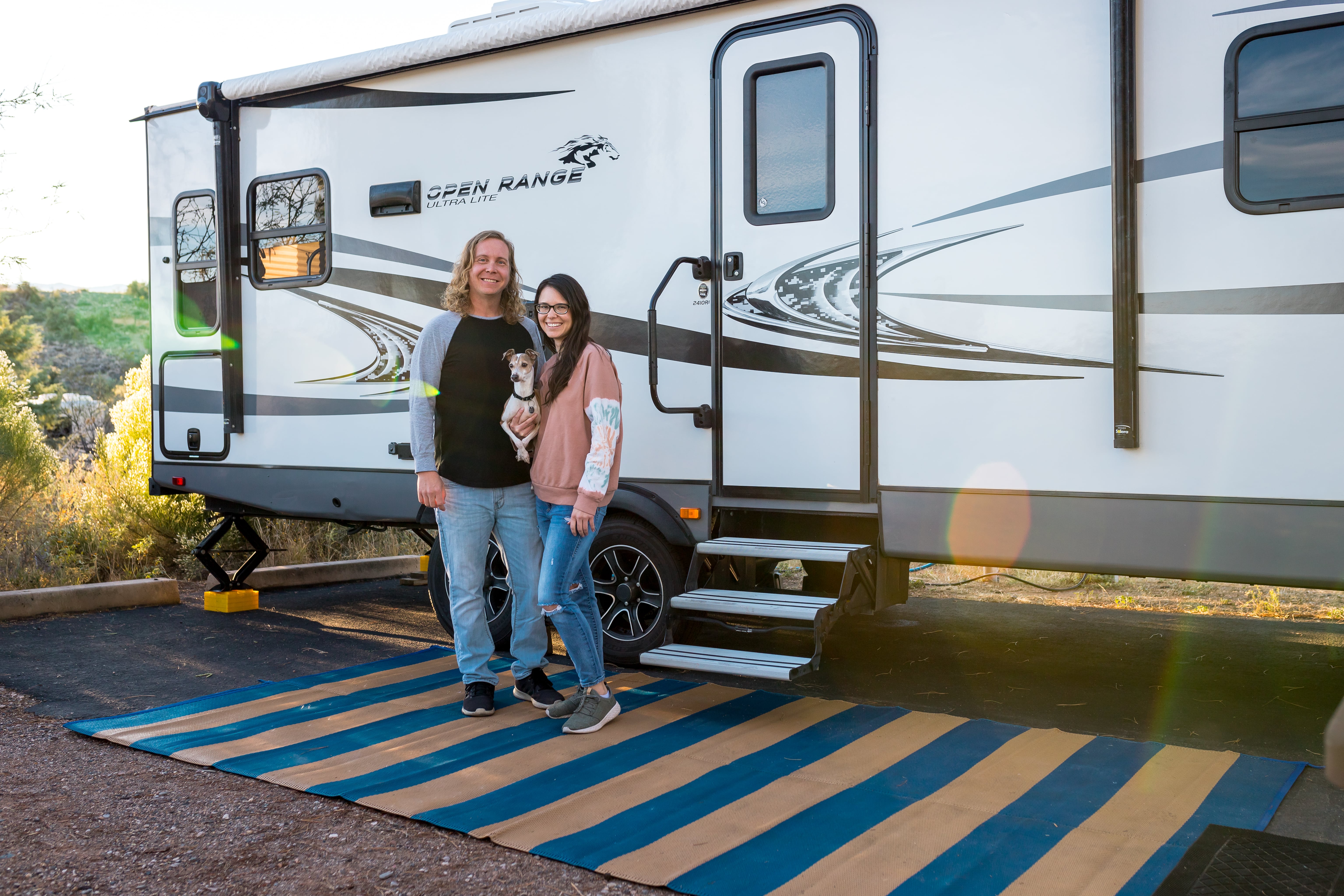A young couple and their small doc stand outside their Heartland Open Range RV posing for a picture.