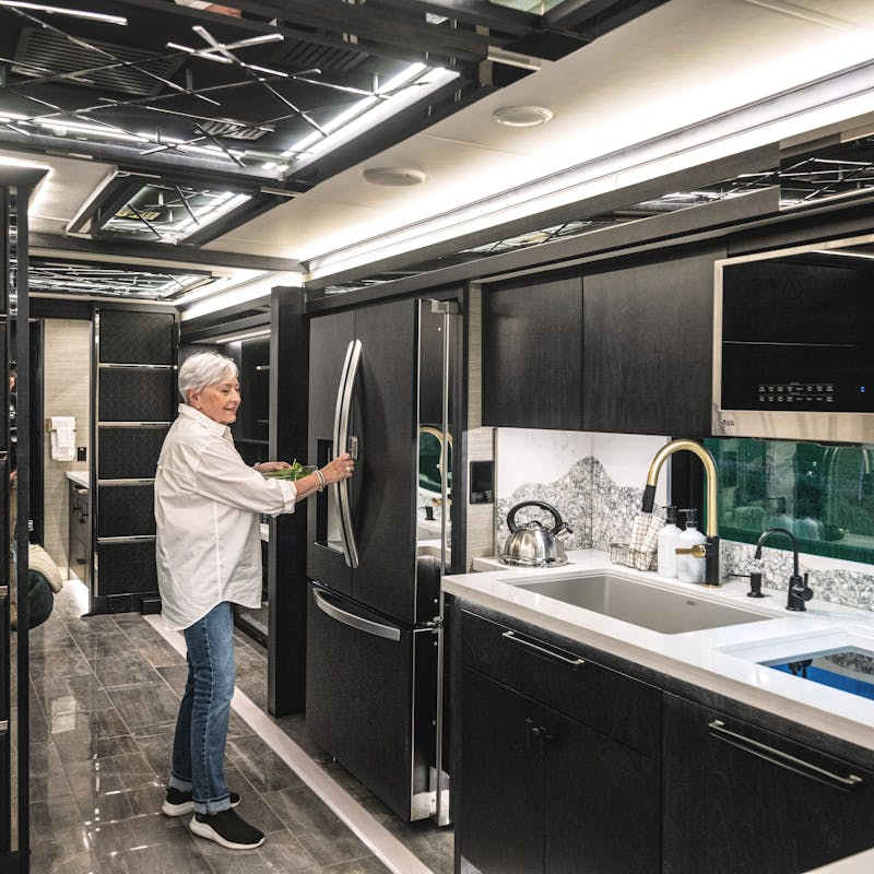 A woman opens a fridge inside the kitchen of a Tiffin Motorhome.
