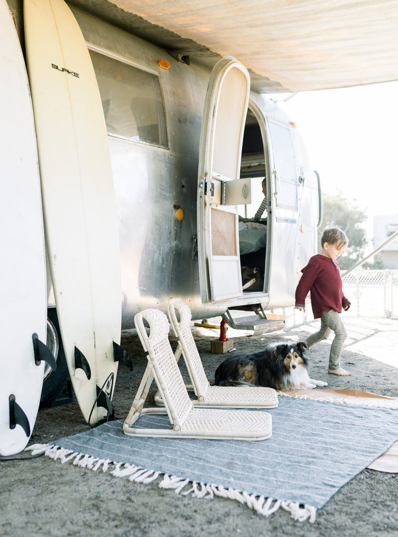 A child leaves through the door of an Airstream RV with two surfboards resting against its side