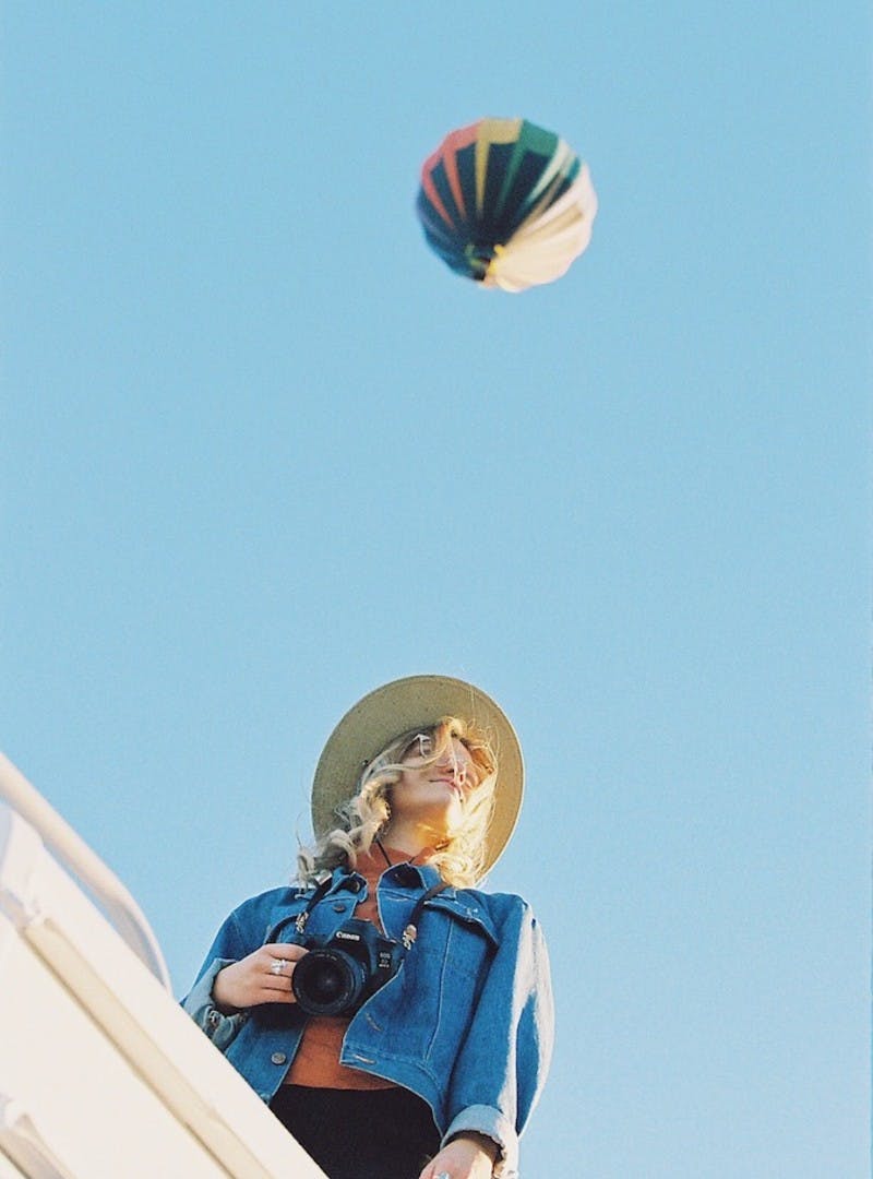 Image looking up at Natalie Allen on top of Entegra Class C RV with a hot air balloon in the sky. 