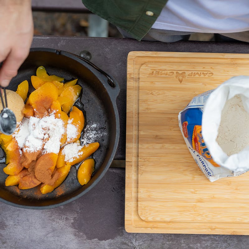 Sprinkling flour over peaches in a dutch oven with brown sugar and cinnamon.
