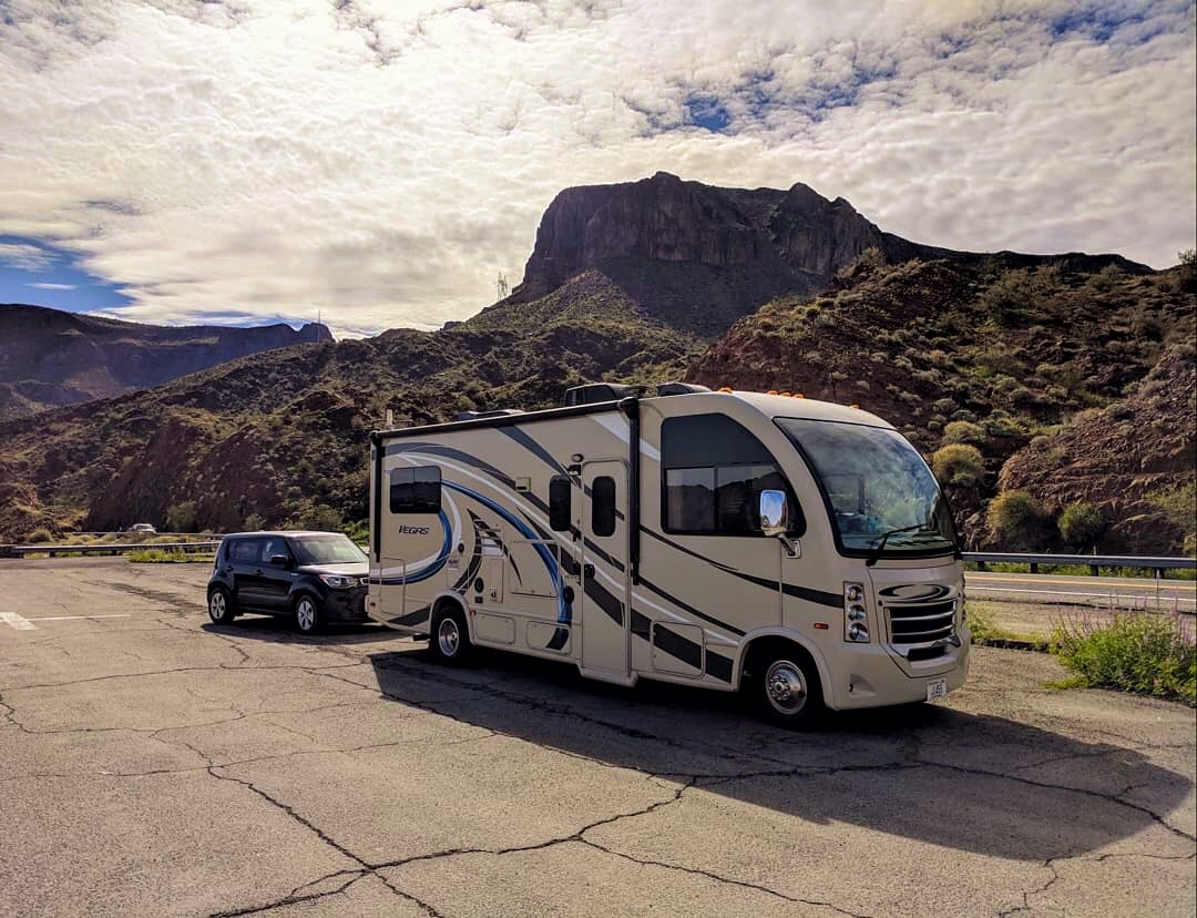 An RV towing a car, parked with a mountain in the background. 