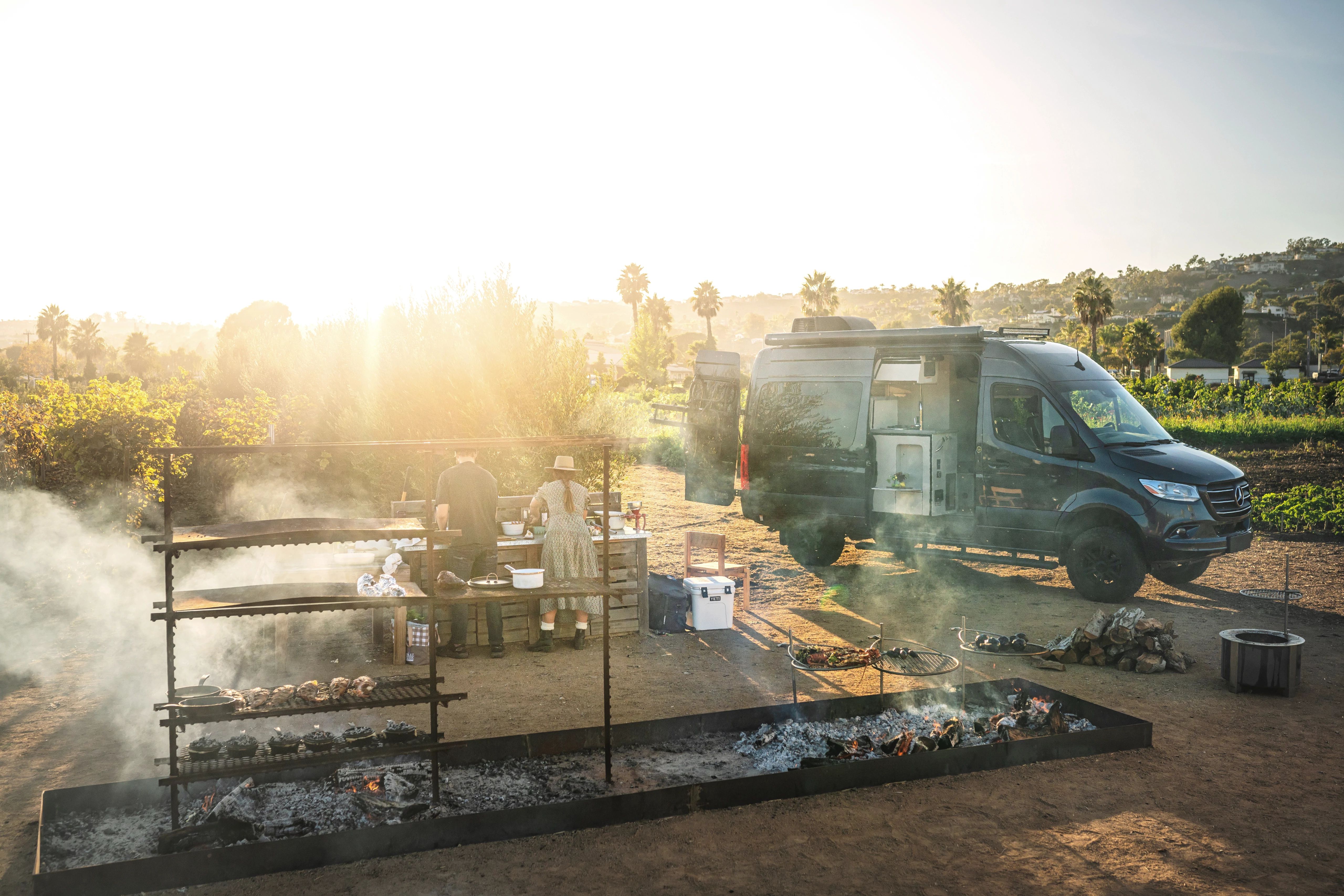 Sarah glover preparing a large meal over an open fire with a class b camper van in the background