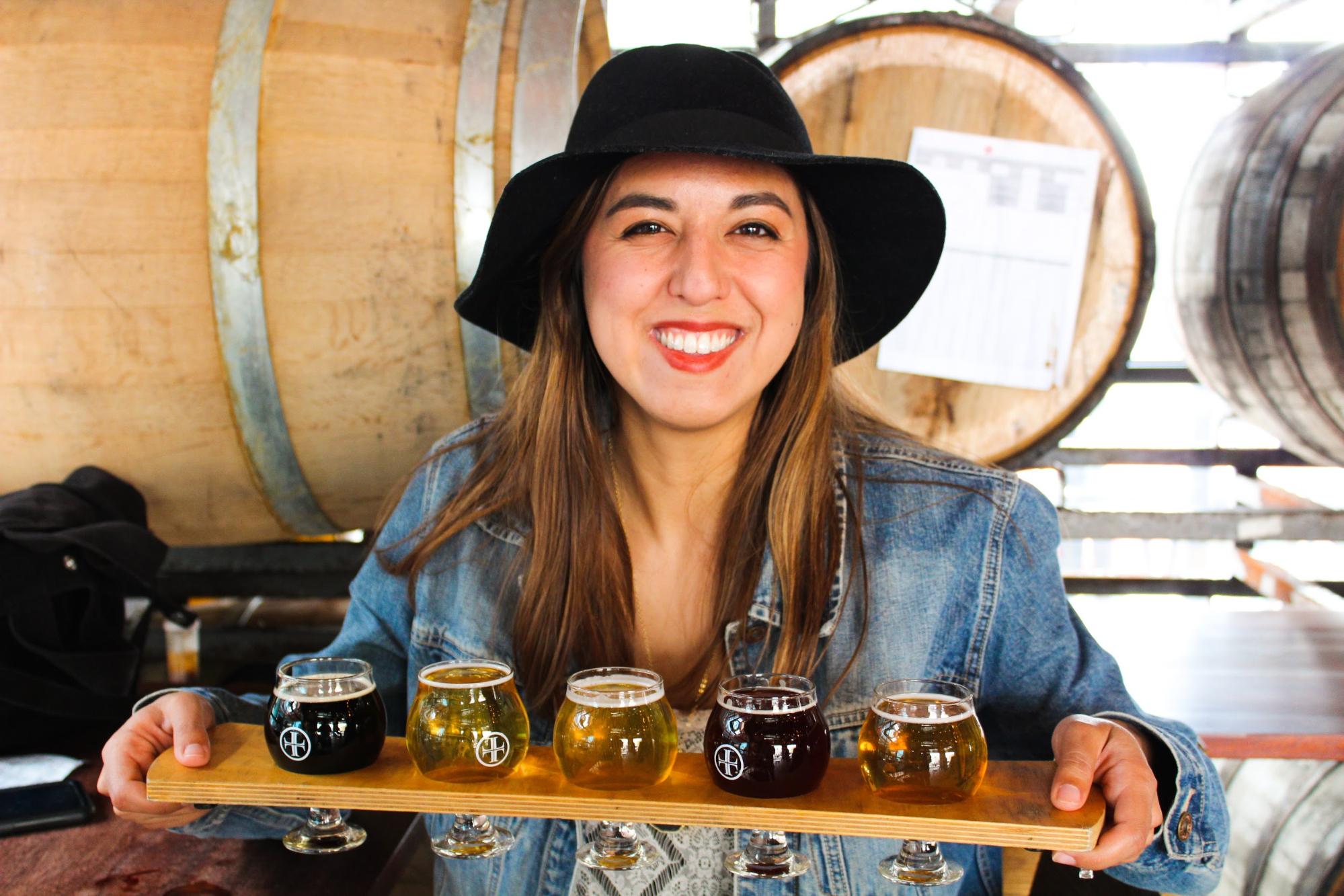 Rachael Lyons smiles holding up a beer flight.