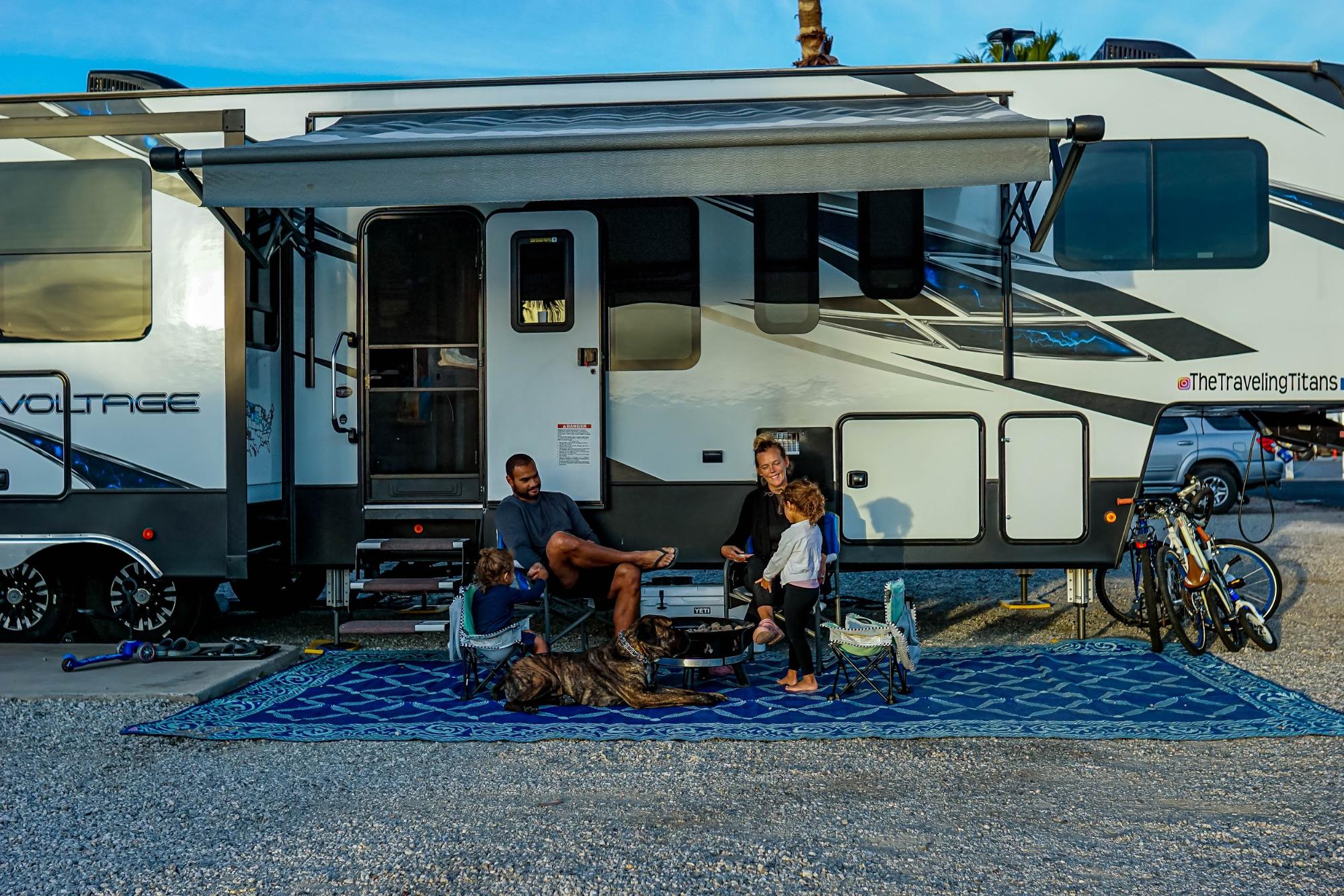Samantha and Blake sit under the awning of their Dutchmen Voltage with two children.