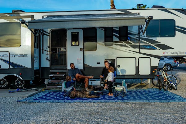 Samantha and Blake sit under the awning of their Dutchmen Voltage with two children.