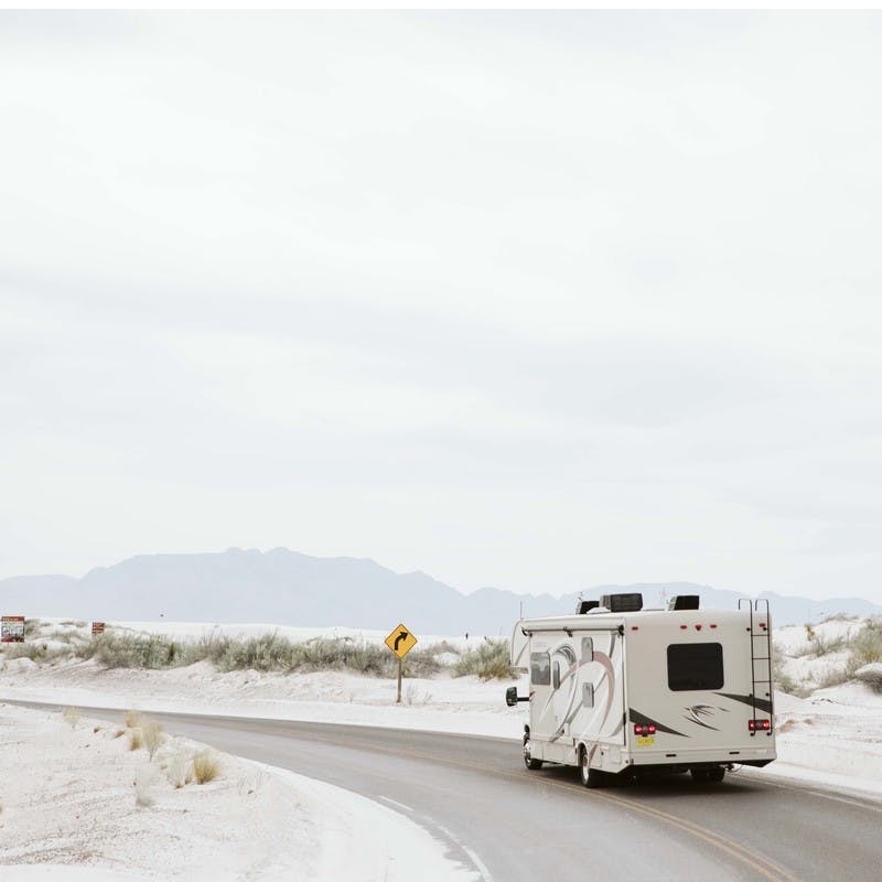 Class C motorhome drives on sandy road through White Sands National Park in New Mexico.
