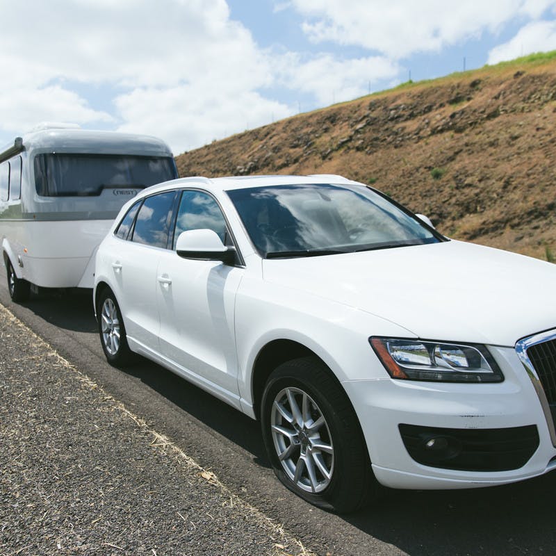 A white car towing an Airstream Nest stuck on the road with a flat tire.