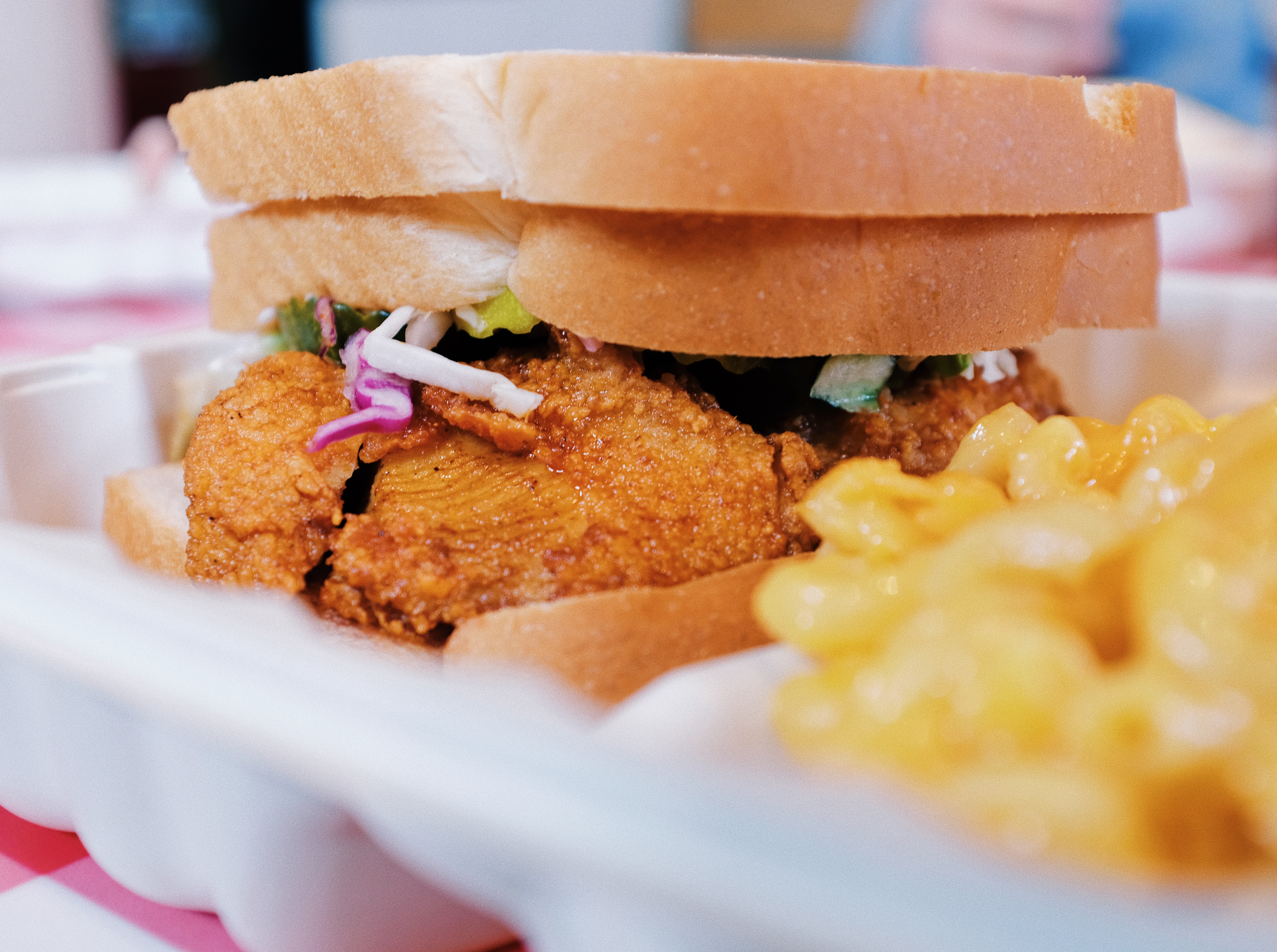 Close up of fried chicken sandwich with slaw and side of mac and cheese.