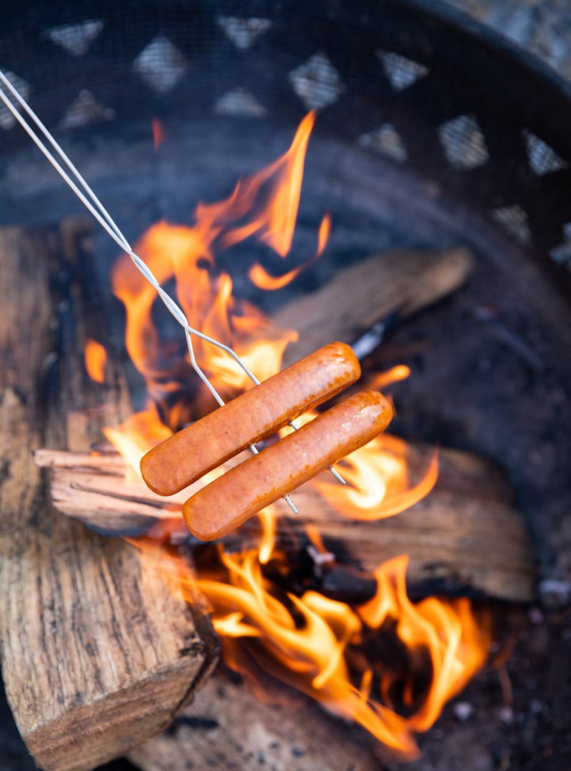 Hot dogs cook over an open fire on a skewer.