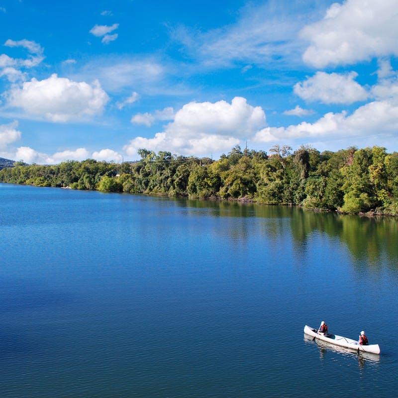 Two people canoeing on the placid blue waters of Lady Bird Lake. 