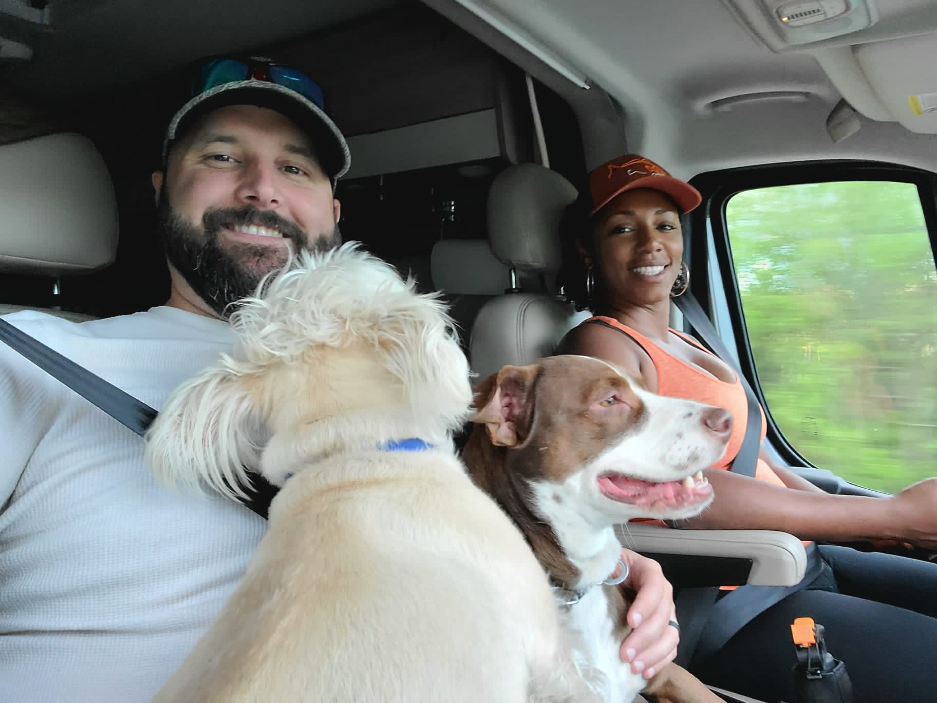 Rocio and Gabe drivin down the road with their two dogs in Gabe's lap.