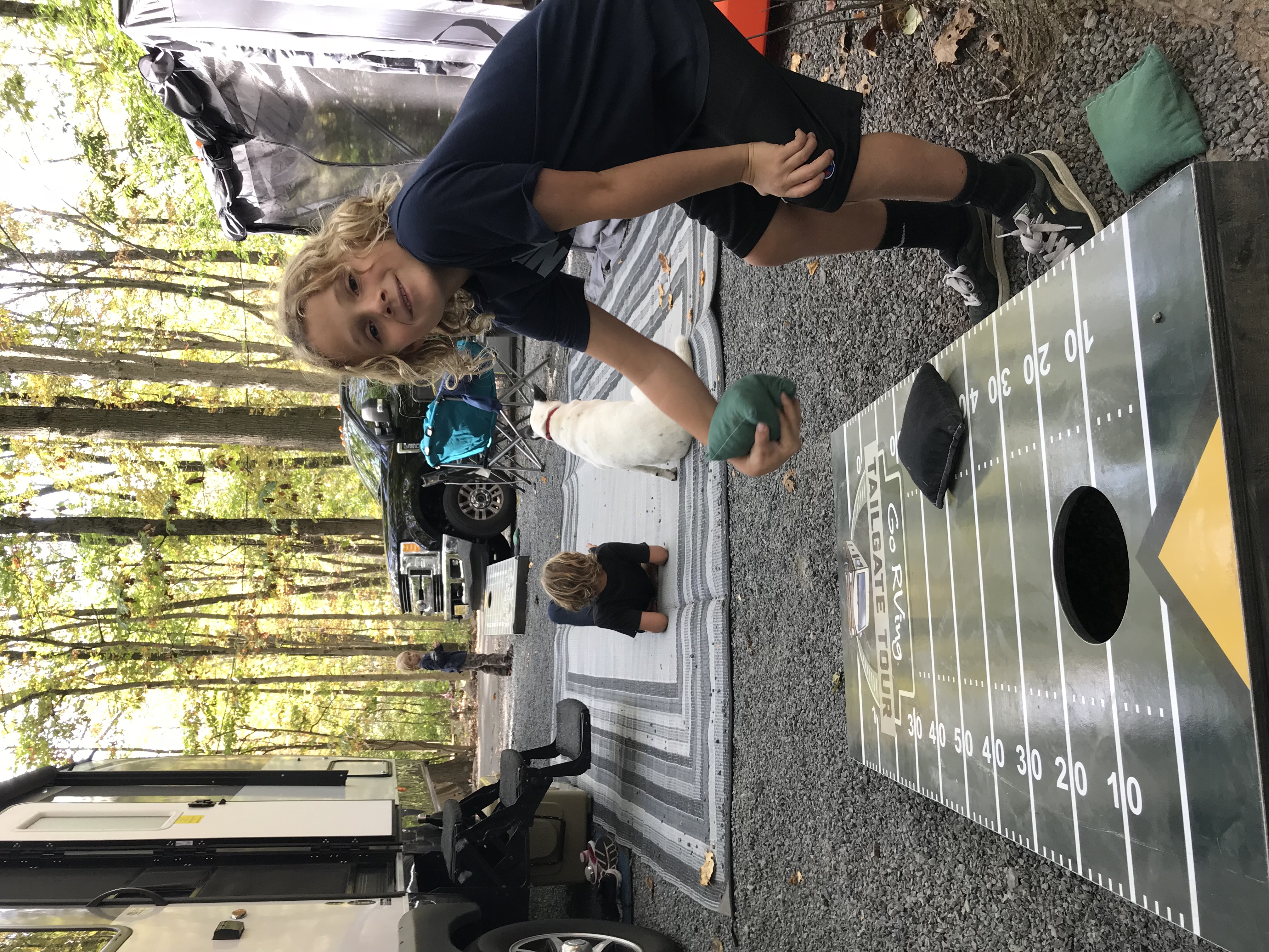 A young boy playing cornhole at a camp site.