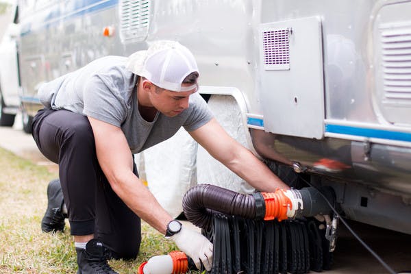 A man hooking up a waste hose to an RV for black water drainage.