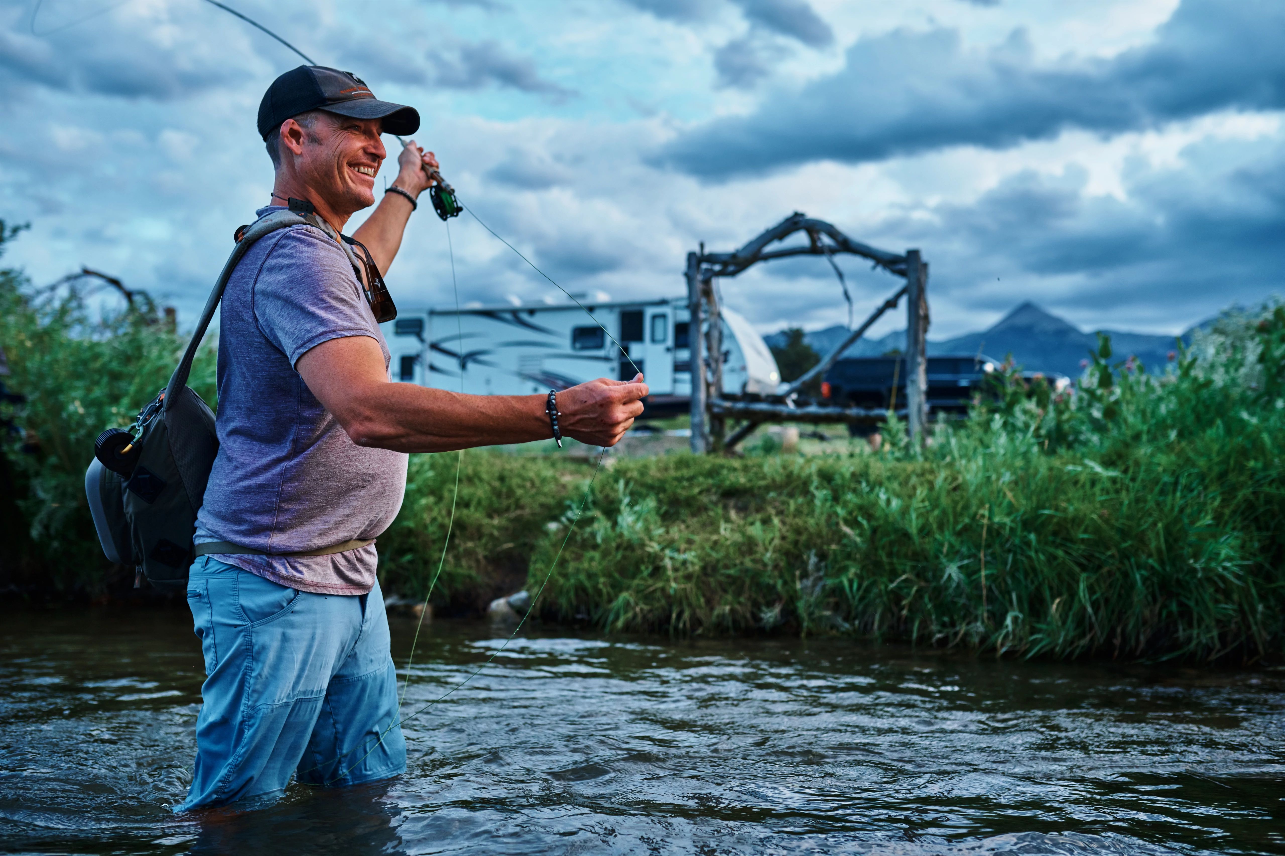 CHRIS HEUBLEIN fishing in a river next to his Keystone Passport RV