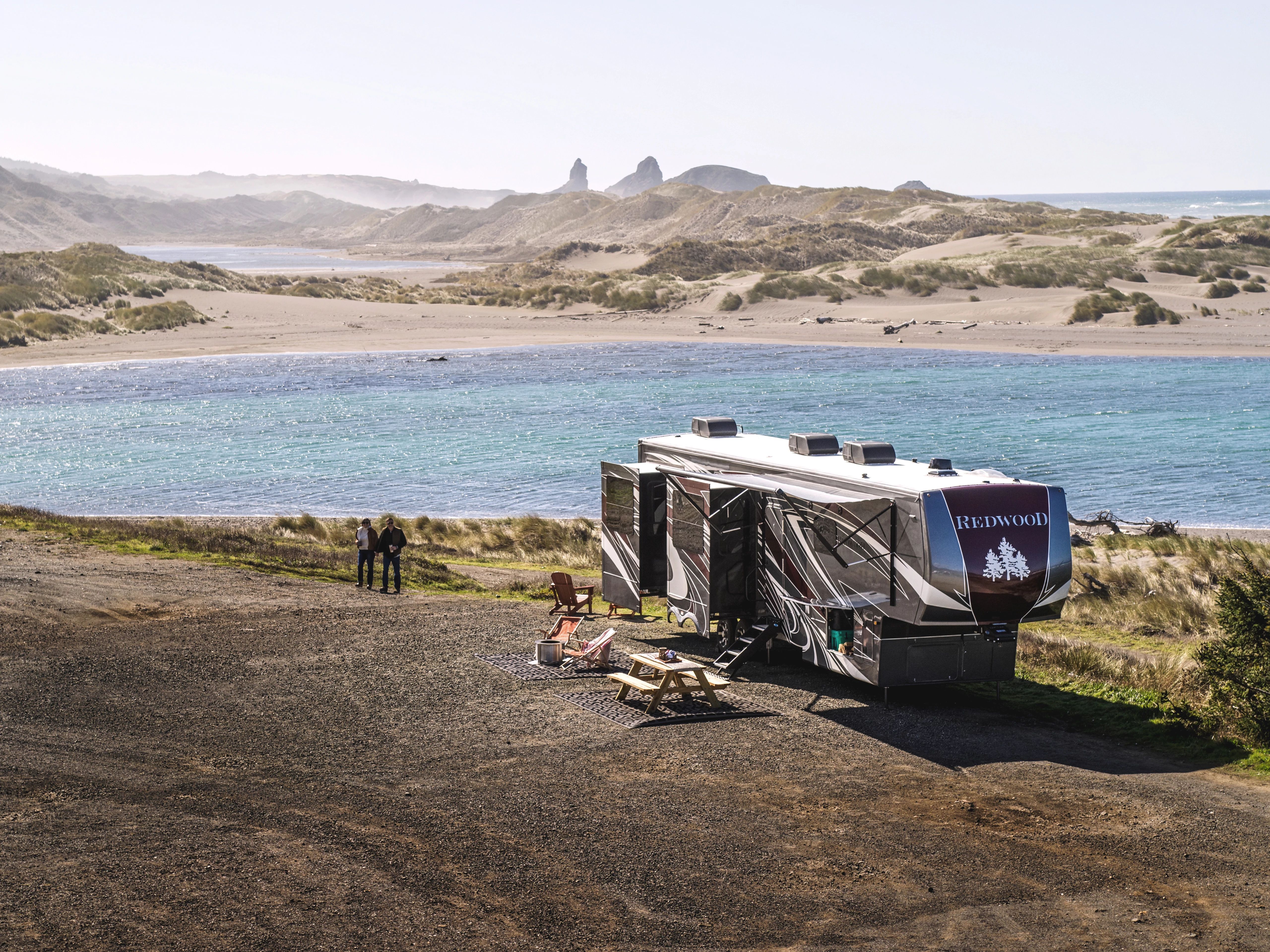 A couple walking near a fifth wheel RV parked on the Oregon coast
