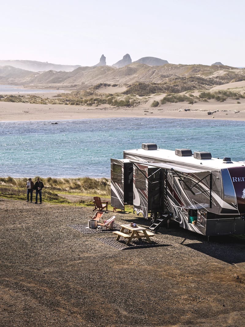 A couple walking near a fifth wheel RV parked on the Oregon coast
