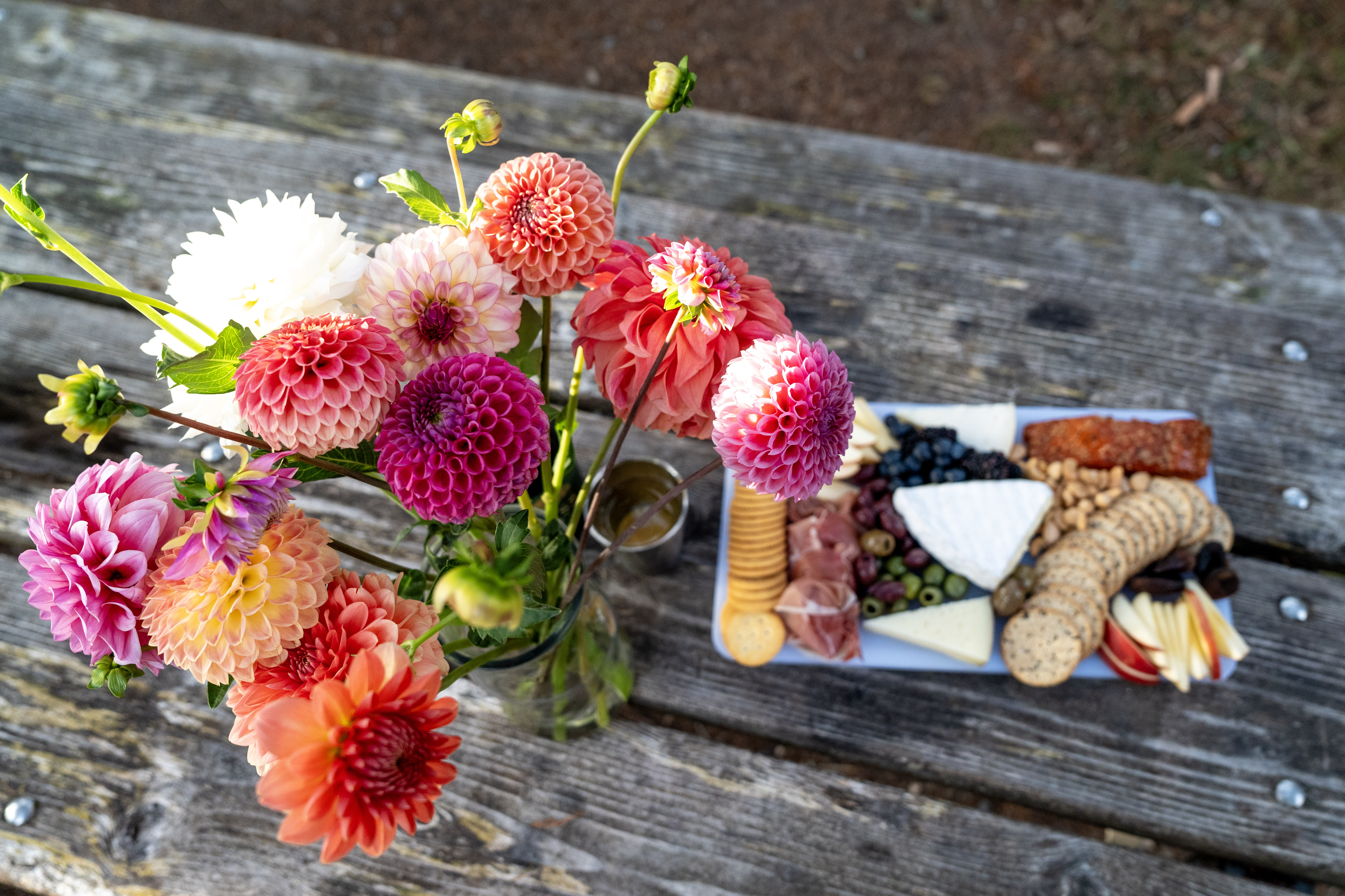 Some flowers and a charcuterie board on a picnic table.