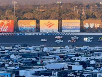 Race cars on the track circling the infield RV camping at the Charlotte Motor Speedway.