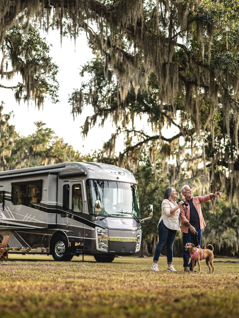 A couple and their dog stand outside a Entegra Cornerstone Class A motorhome.