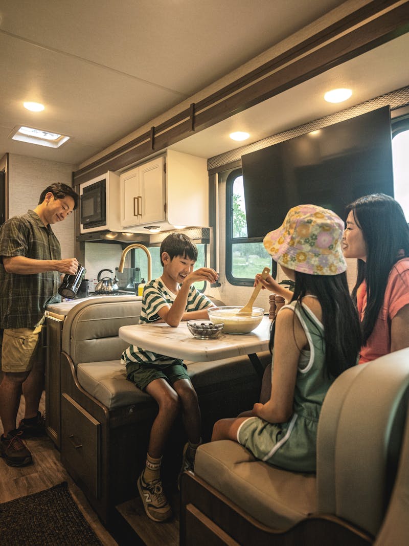 A family eats at a dinette in a Thor Motor Coach Four Winds motorhome.