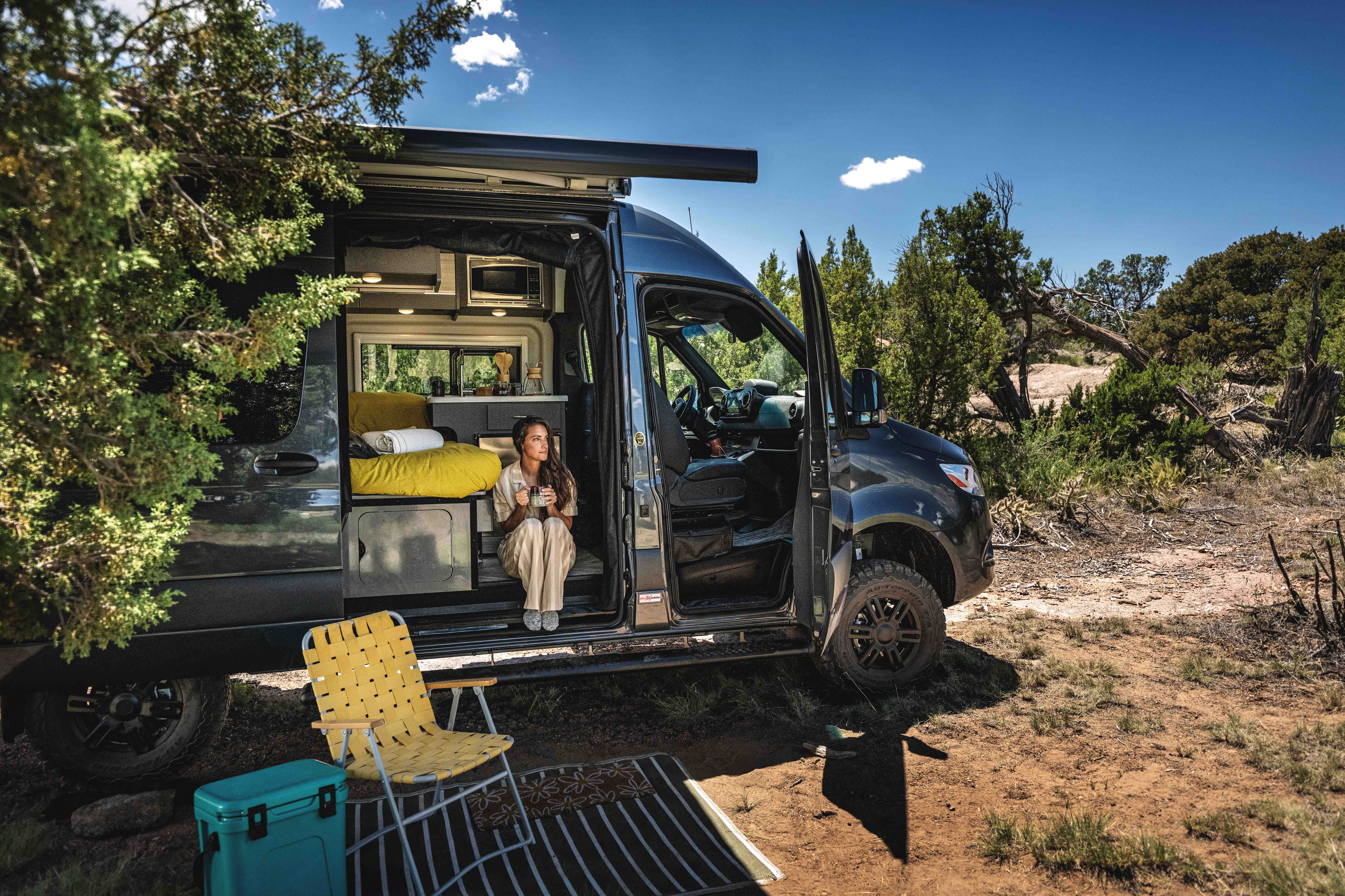A woman sits inside a Thor Motor Coach Tranquility at a campsite.