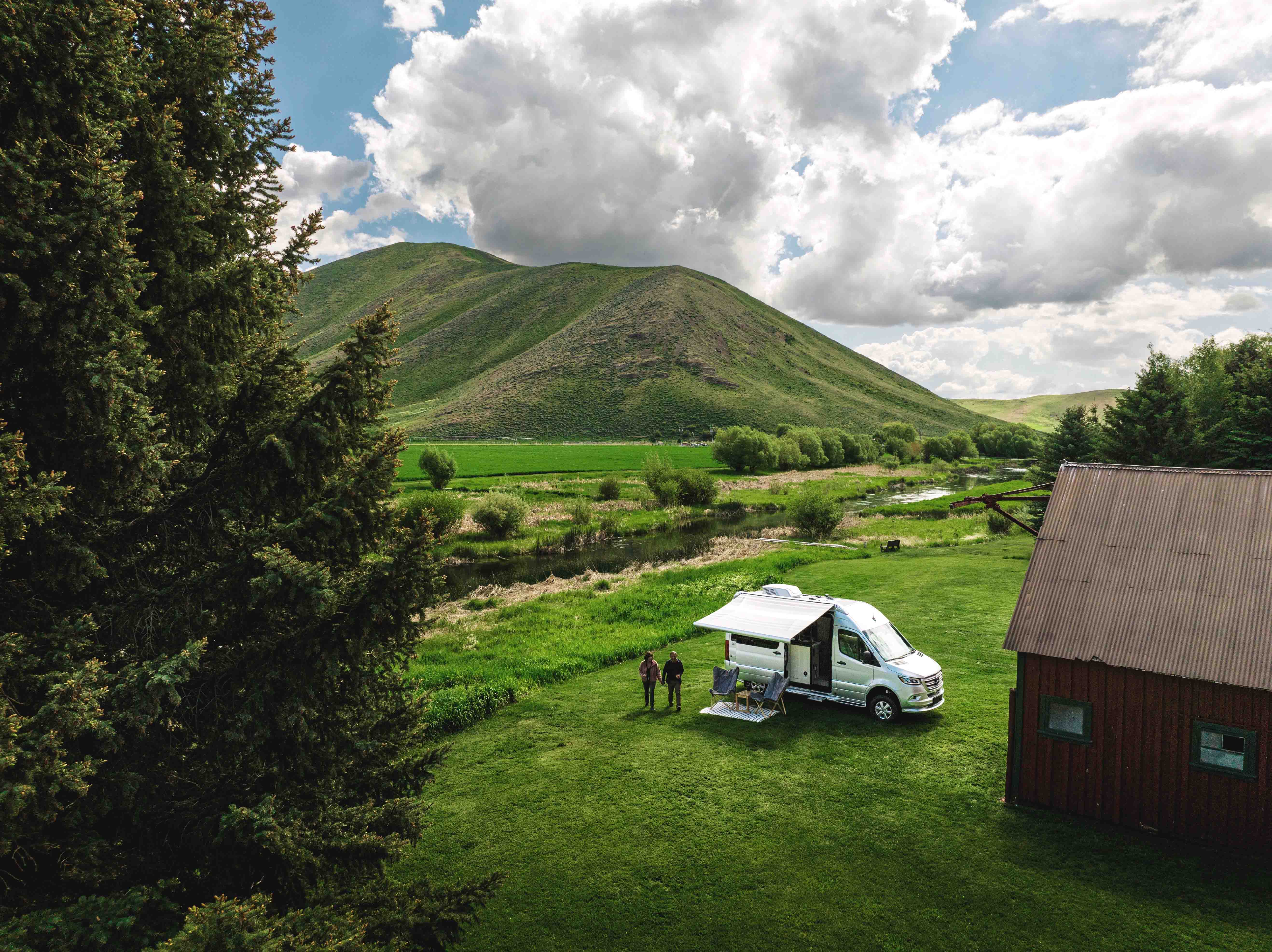 An Airstream Interstate camper van at a grassy campsite next to mountains.