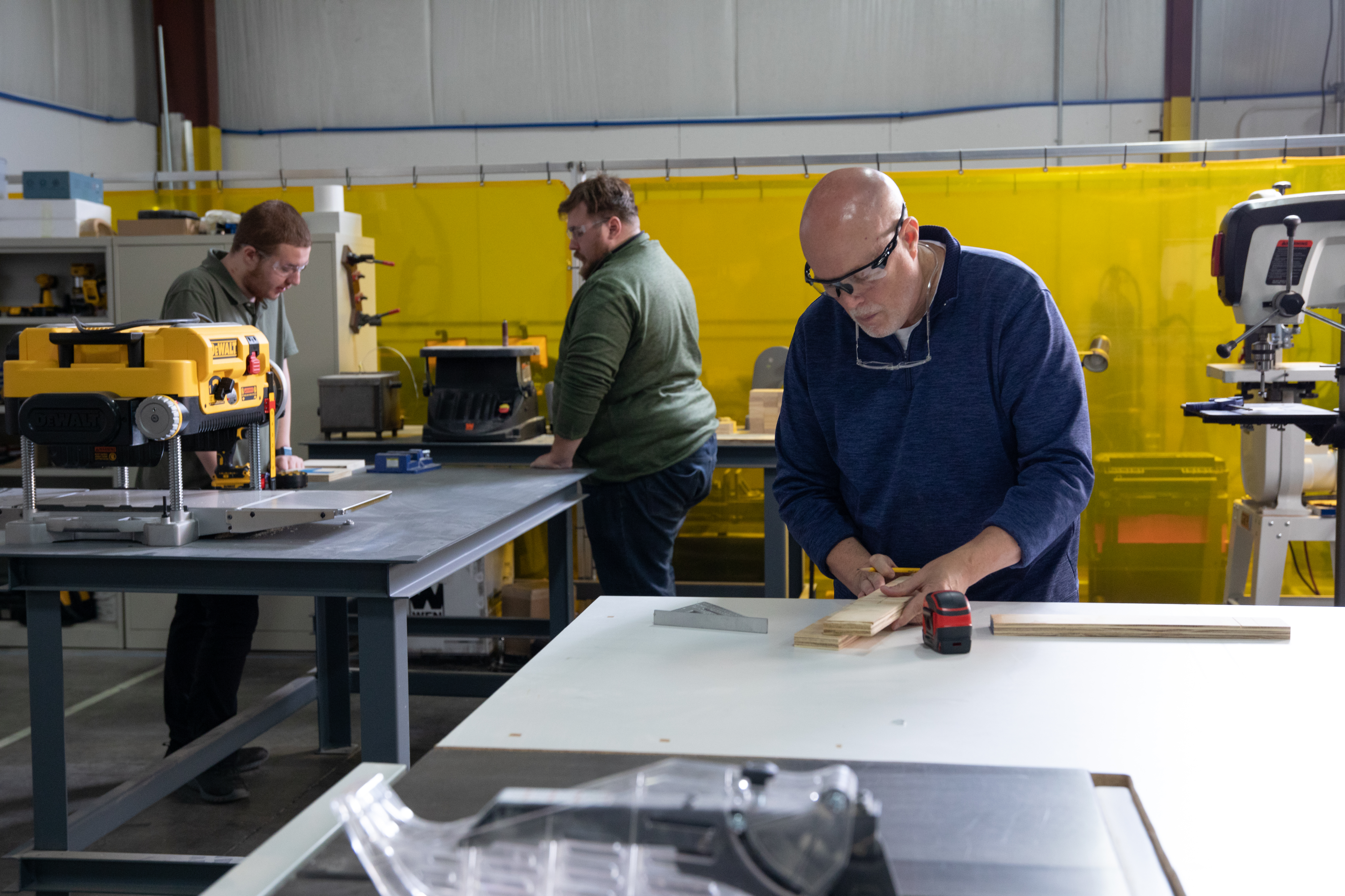 THOR Industries team members measure and cut pieces of wood at a working table.