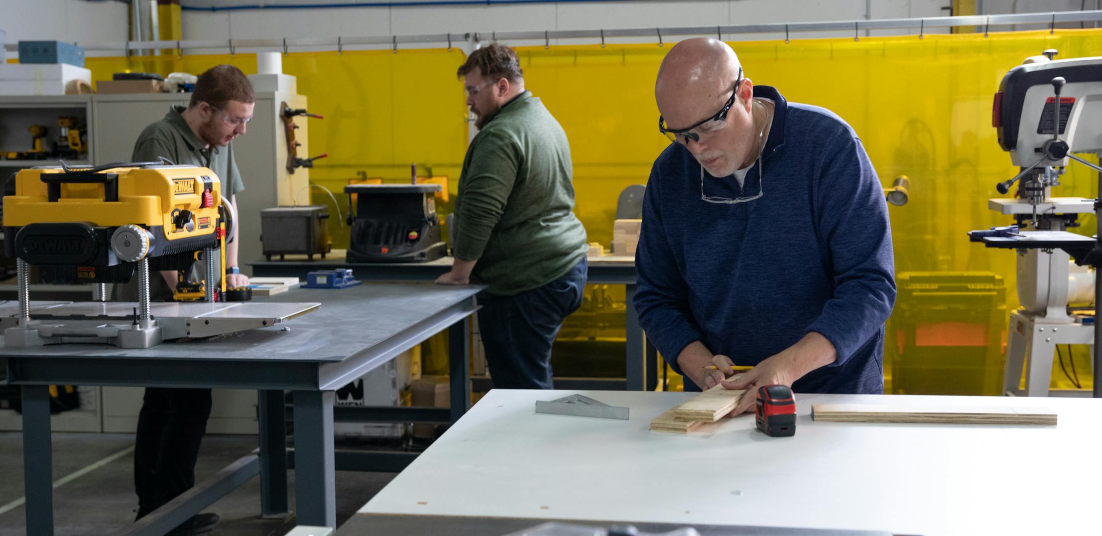 THOR Industries team members measure and cut pieces of wood at a working table.