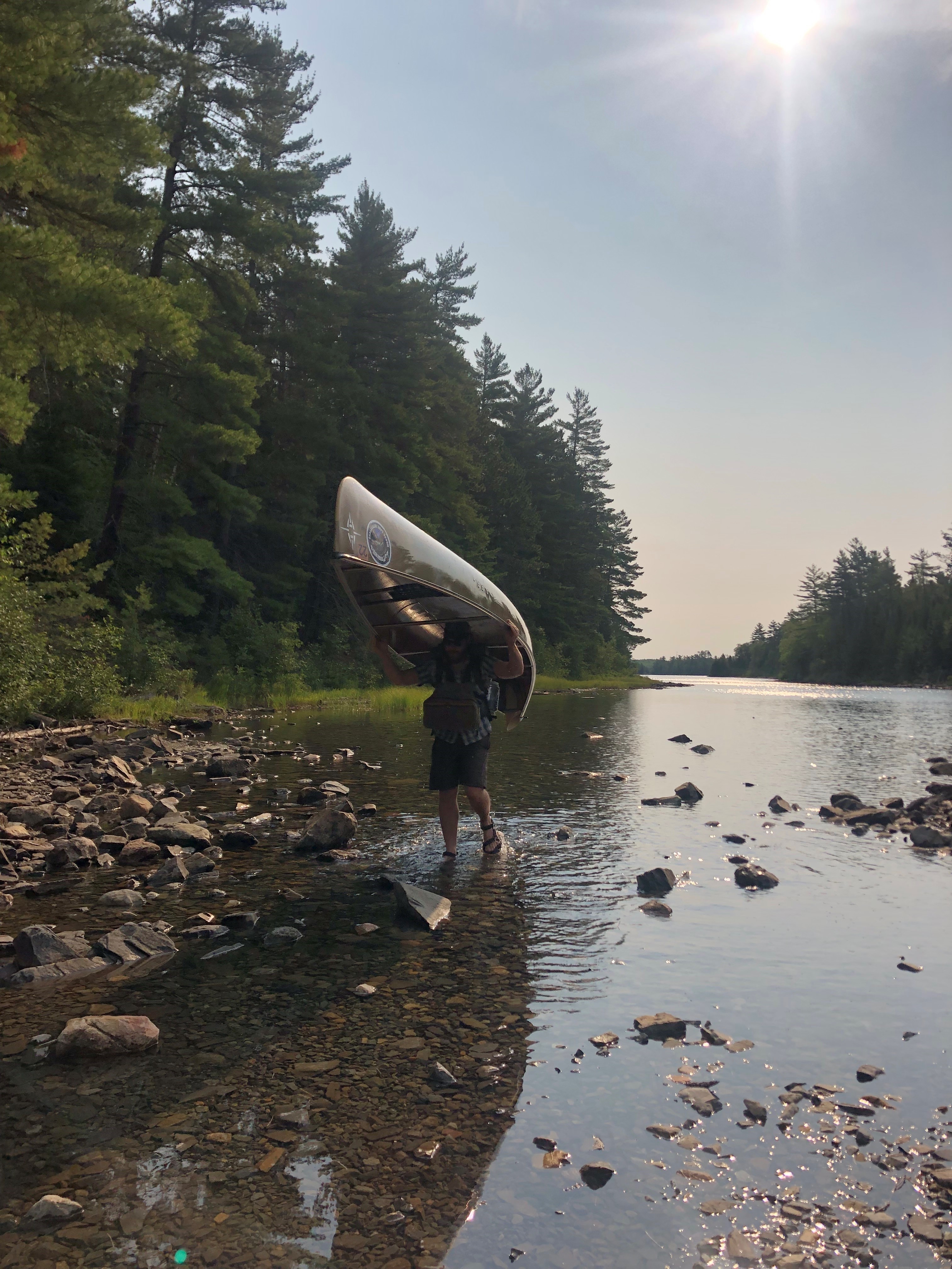 A person walks along the beach with a canoe in Superior National Forest.