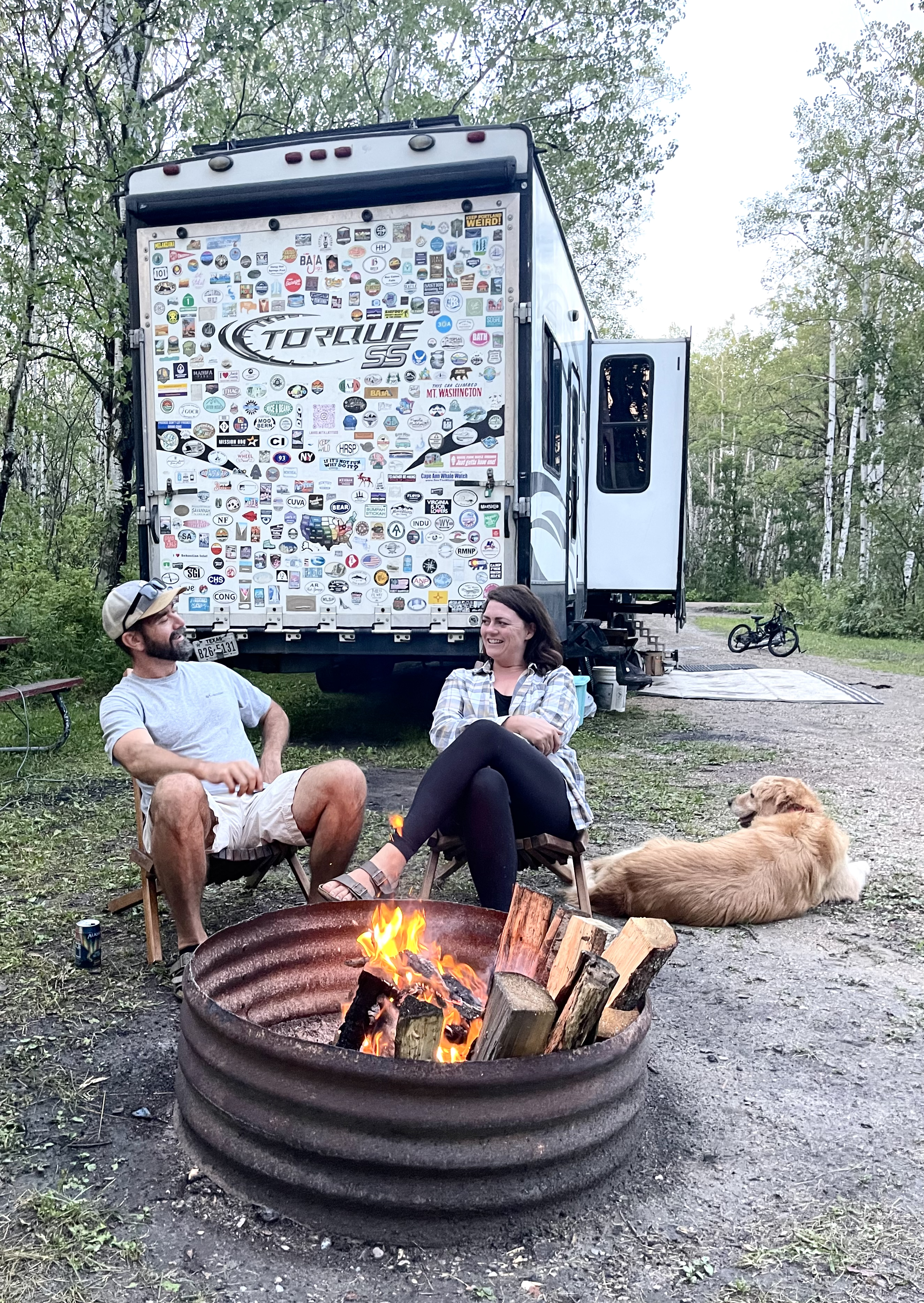Melissa and Lucas Lahr sitting around a bonfire next to their Heartland Torque toy hauler.