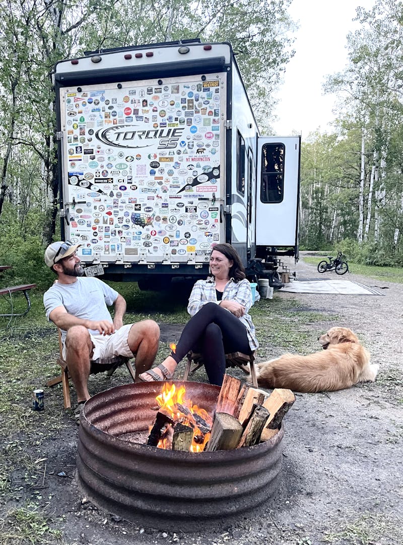 Melissa and Lucas Lahr sitting around a bonfire next to their Heartland Torque toy hauler.