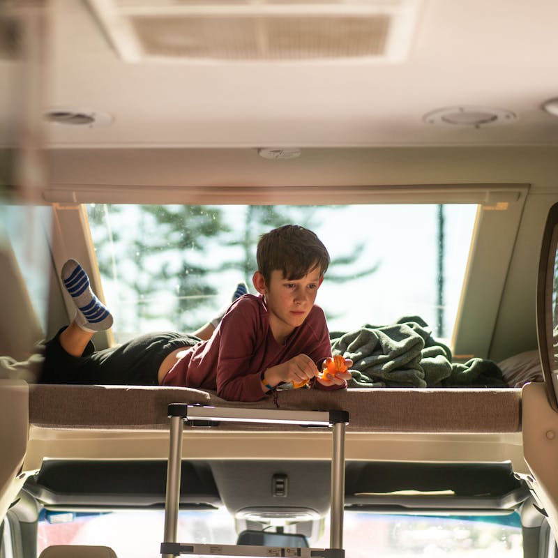 One of the Tilby kids sits in the overhead bunkbed in a rented motorized RV.