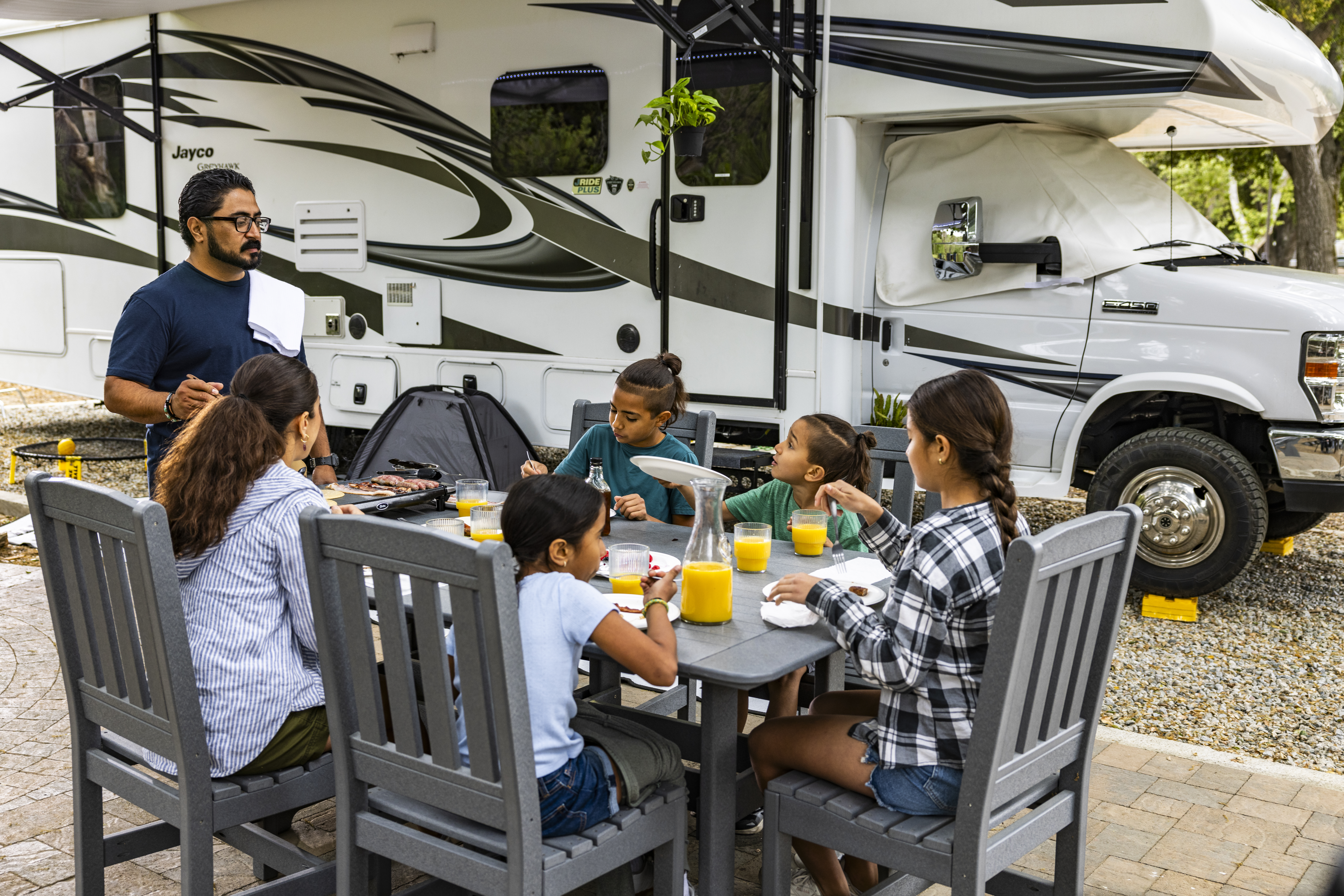 The Peña sit around a table having breakfast outside of their Jayco Greyhawk.