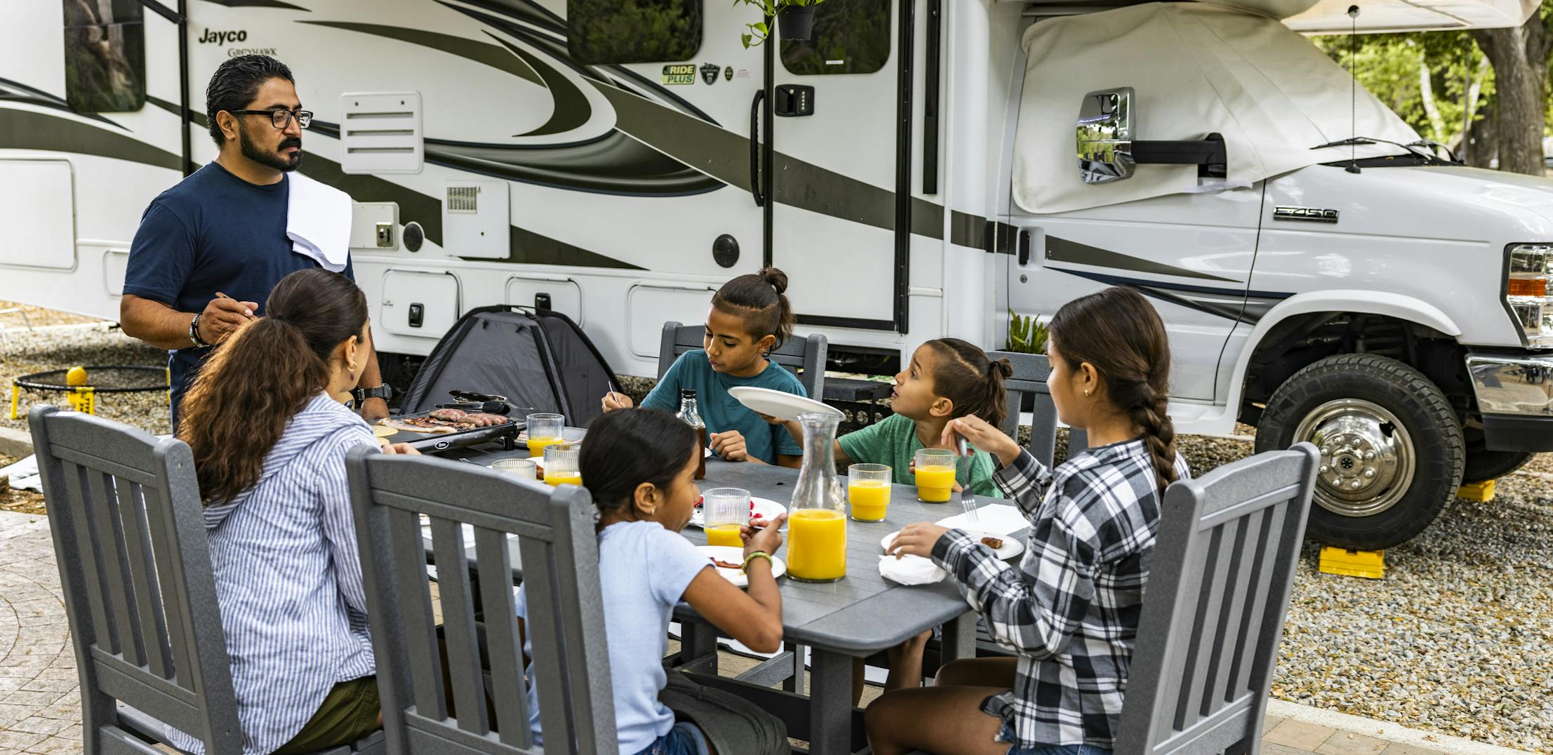 The Peña sit around a table having breakfast outside of their Jayco Greyhawk.