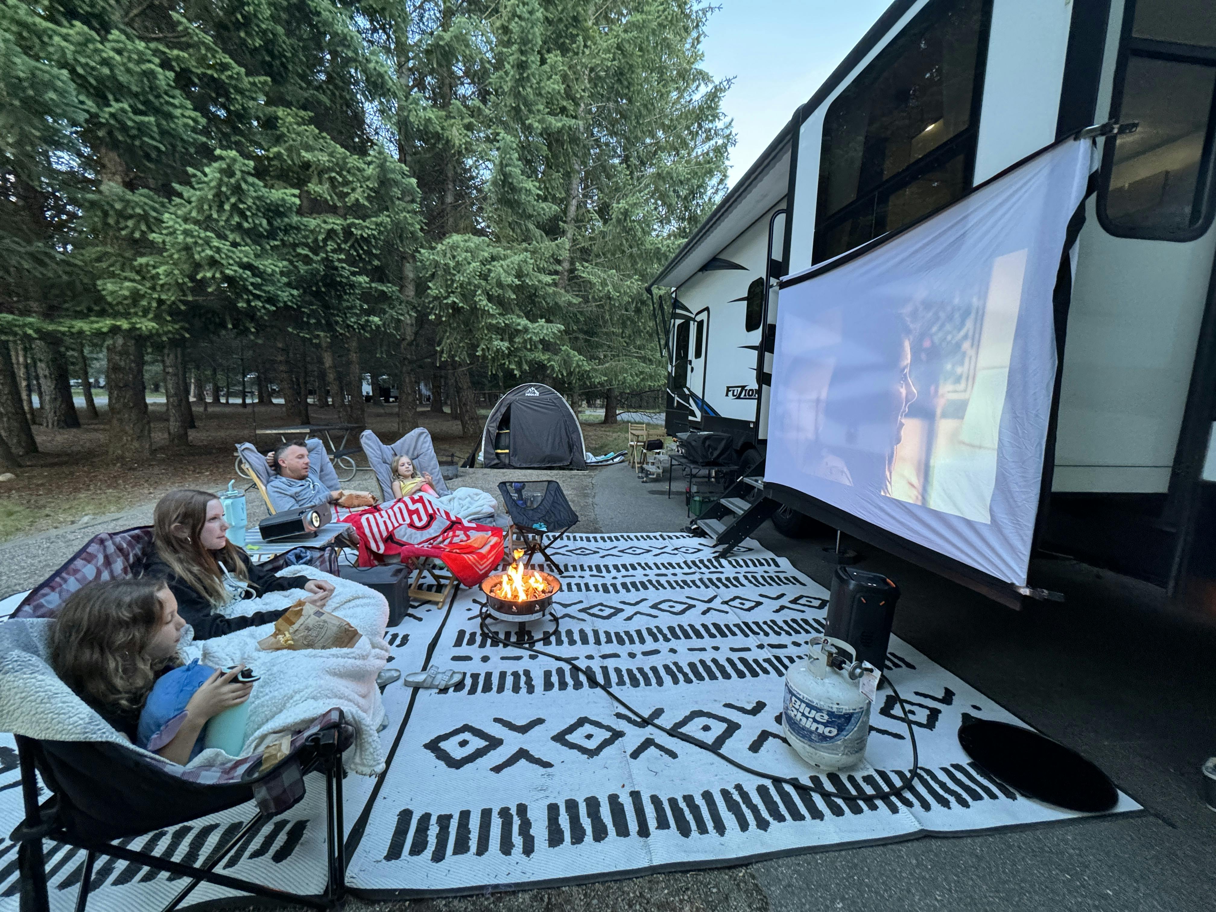 A family sits around a movie screen outside of a Keystone Avalanche fifth wheel.