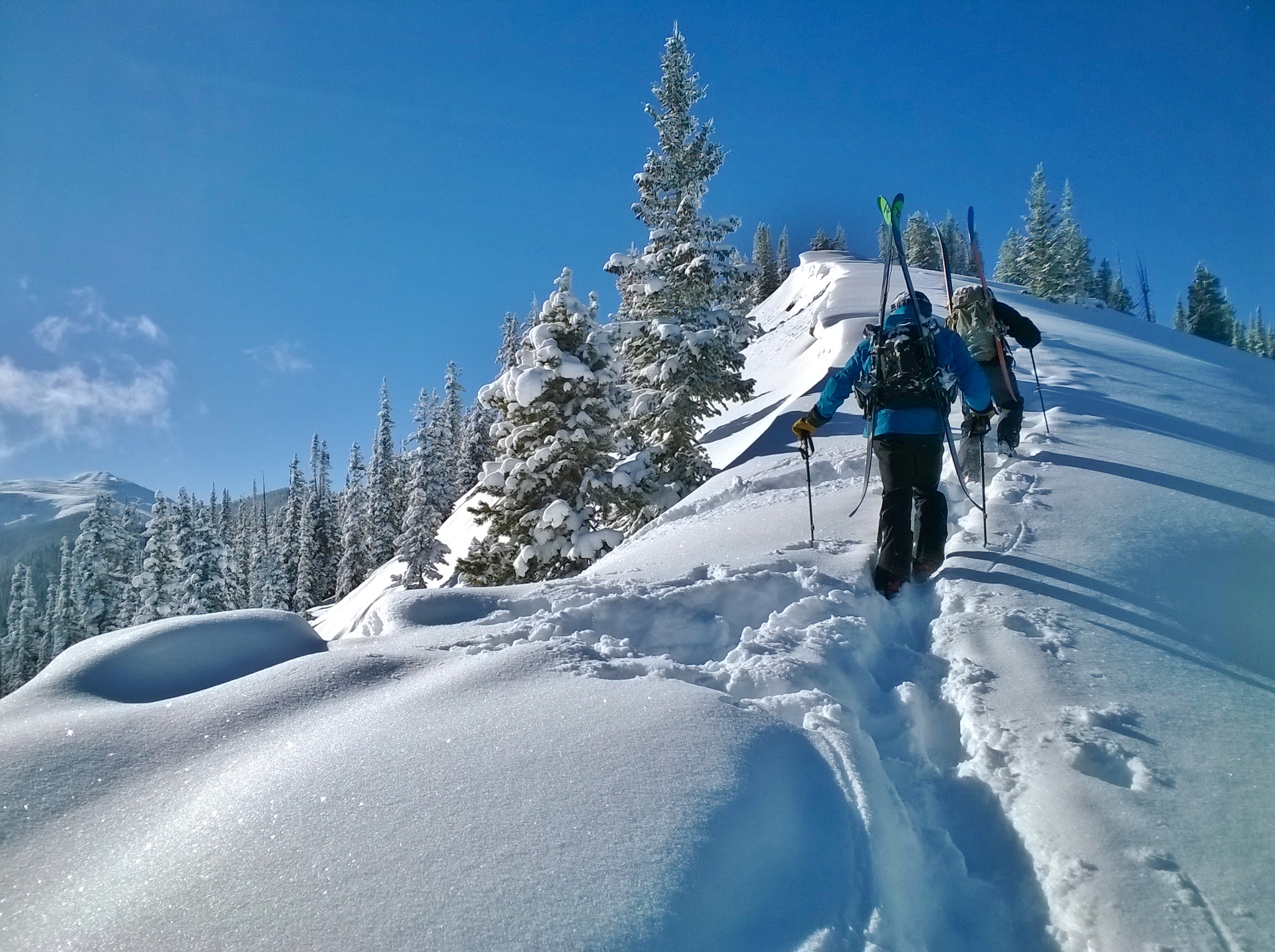Hikers summit a snowy mountain peak in White River National Forest.