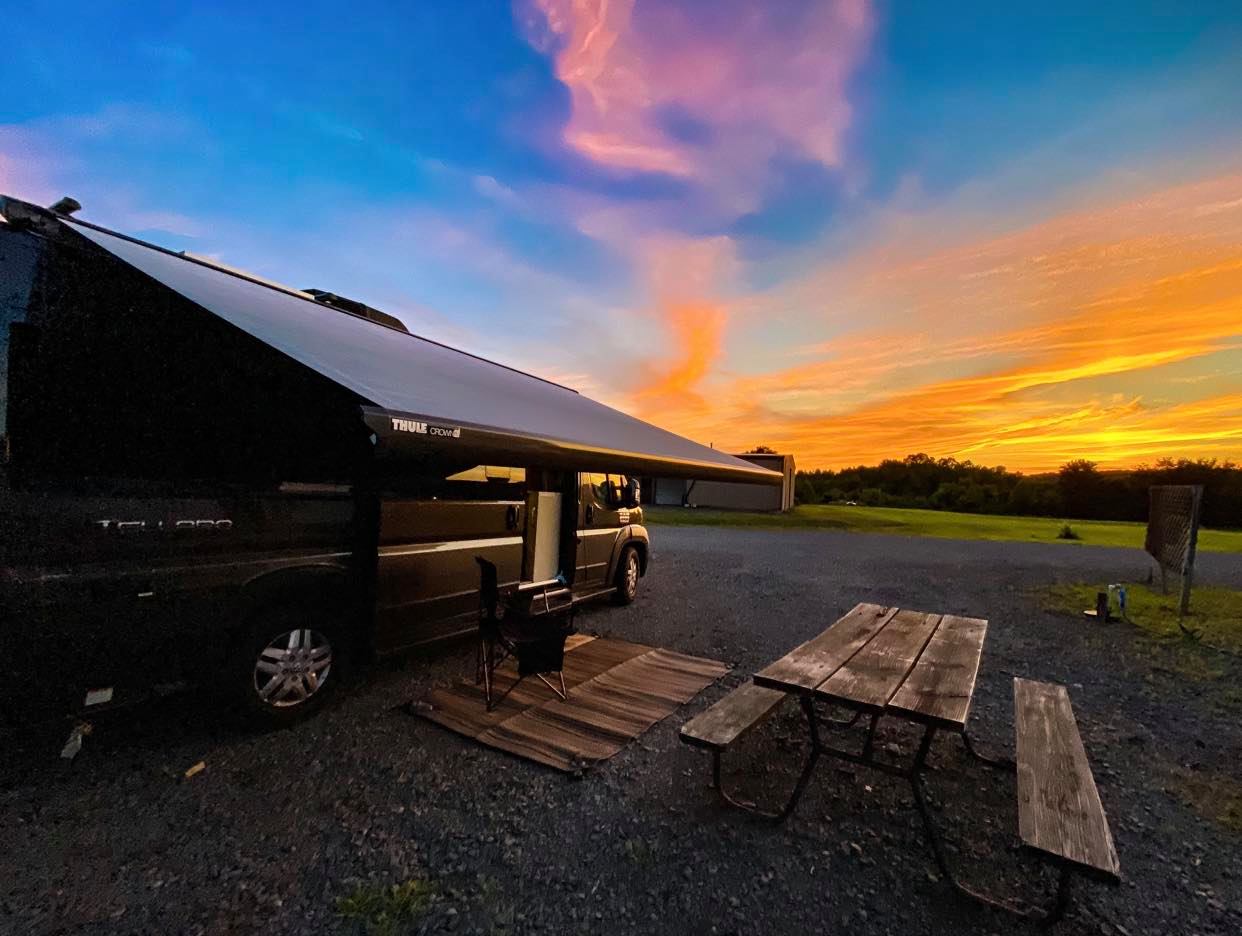 A Class B Van parked by a picnic table under a colorful sunset.