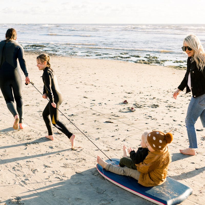 Amber Thrane and her family playing on the beach and pulling a sled with their kids on it.