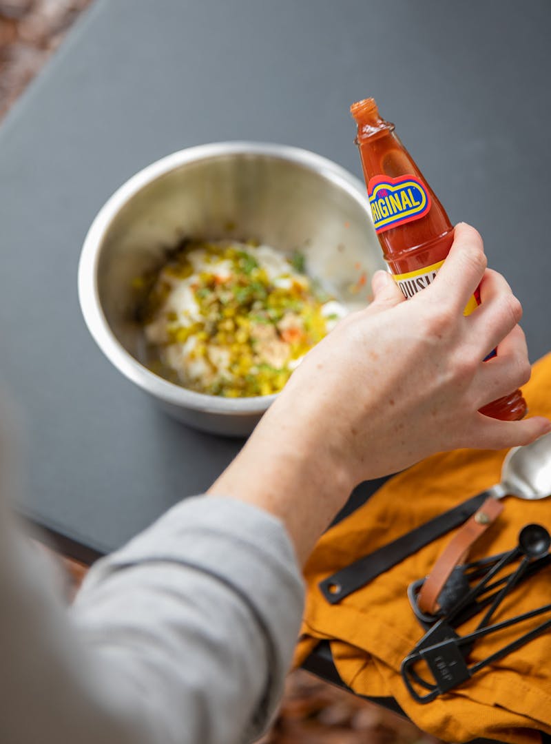 Adding hot sauce to remoulade ingredients.