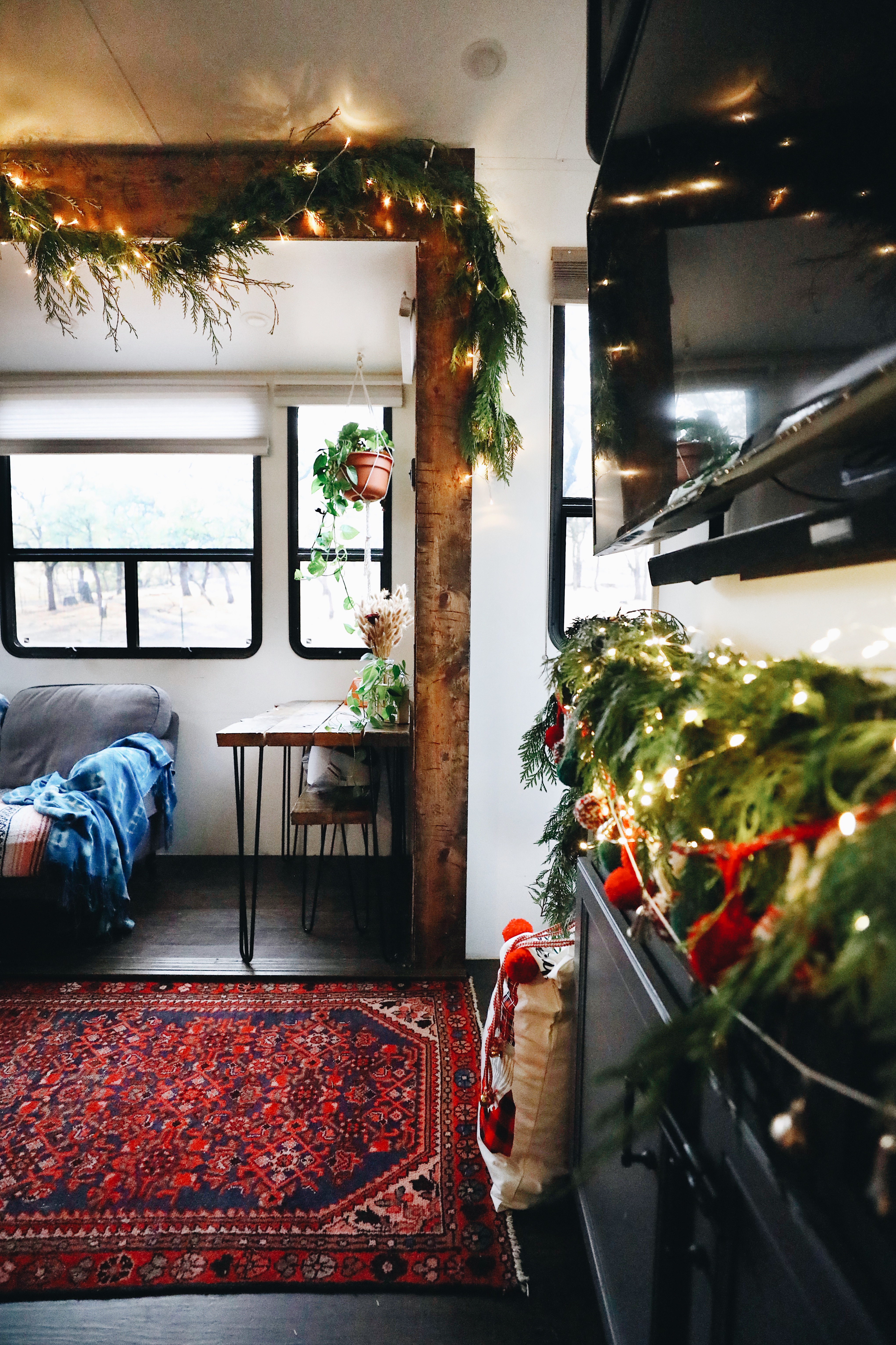 A living area in an RV decorated in pine boughs and Christmas lights. 
