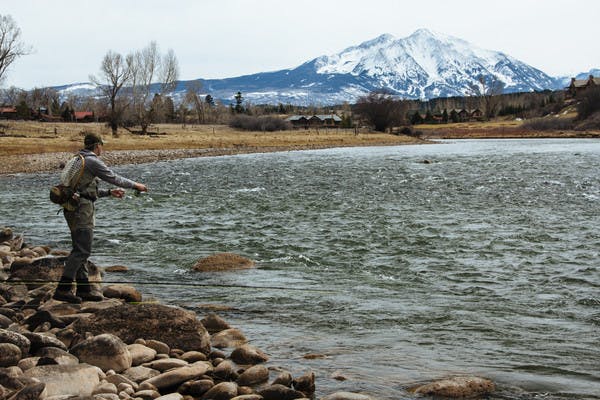 A man fishing on a lake at the base of a mountain. 