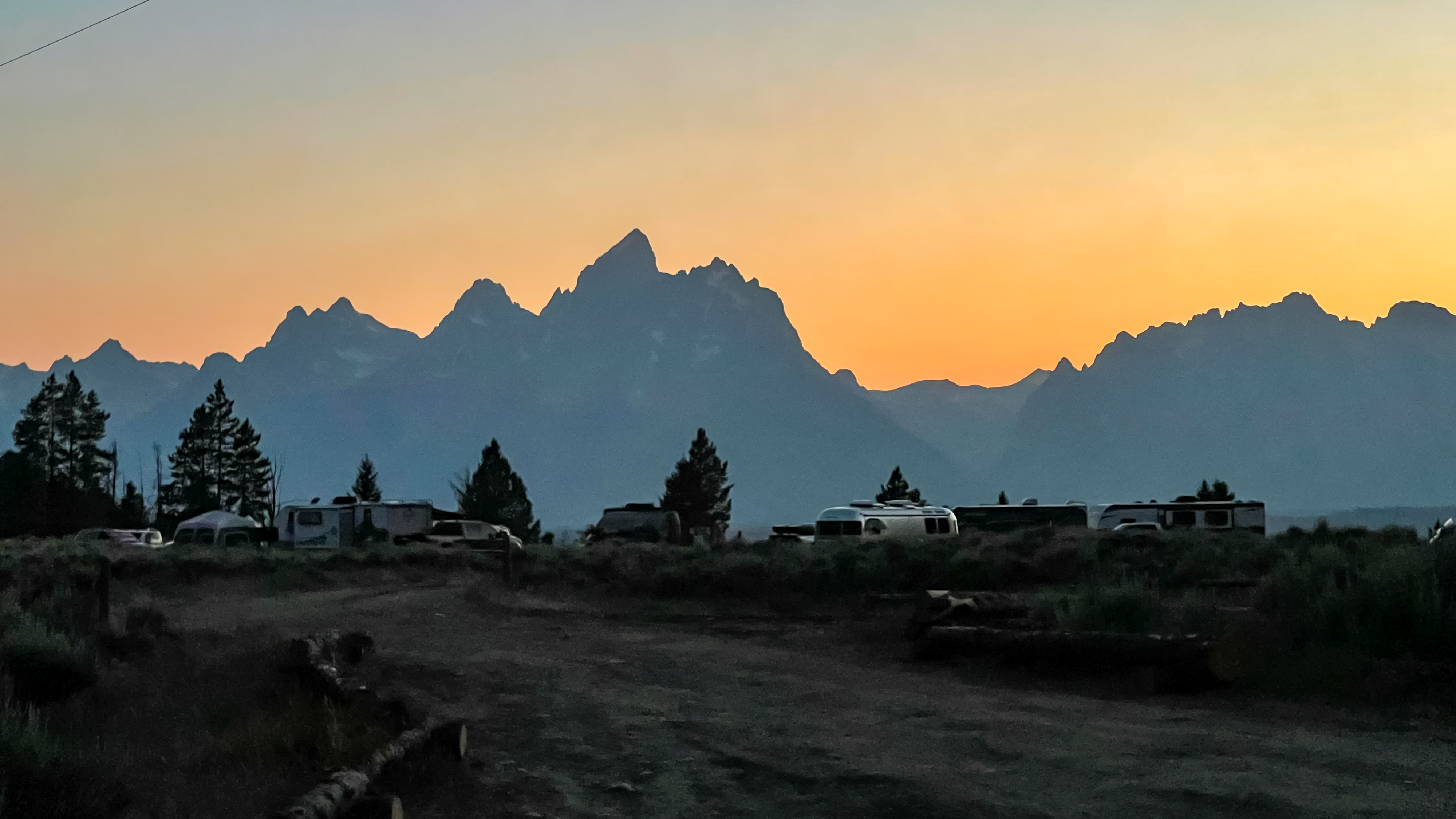A view of RVs parked in a National Forest with the sun going down behind mountains