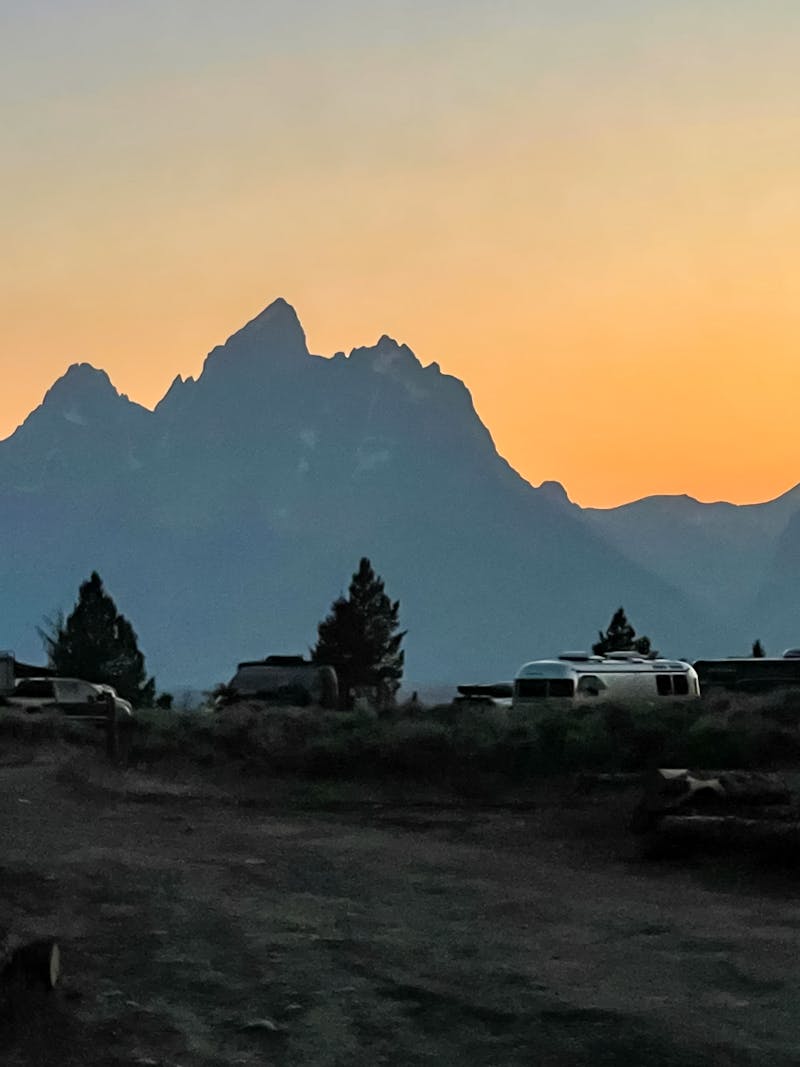 A view of RVs parked in a National Forest with the sun going down behind mountains