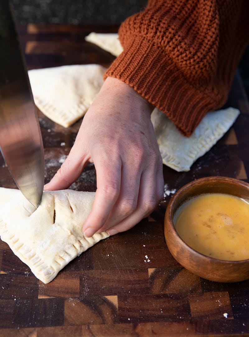 Cutting slits into folded hand pies before brushing with egg wash.