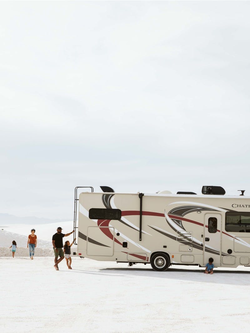 Family of four walking around large Class C motorhome at White Sands in New Mexico.