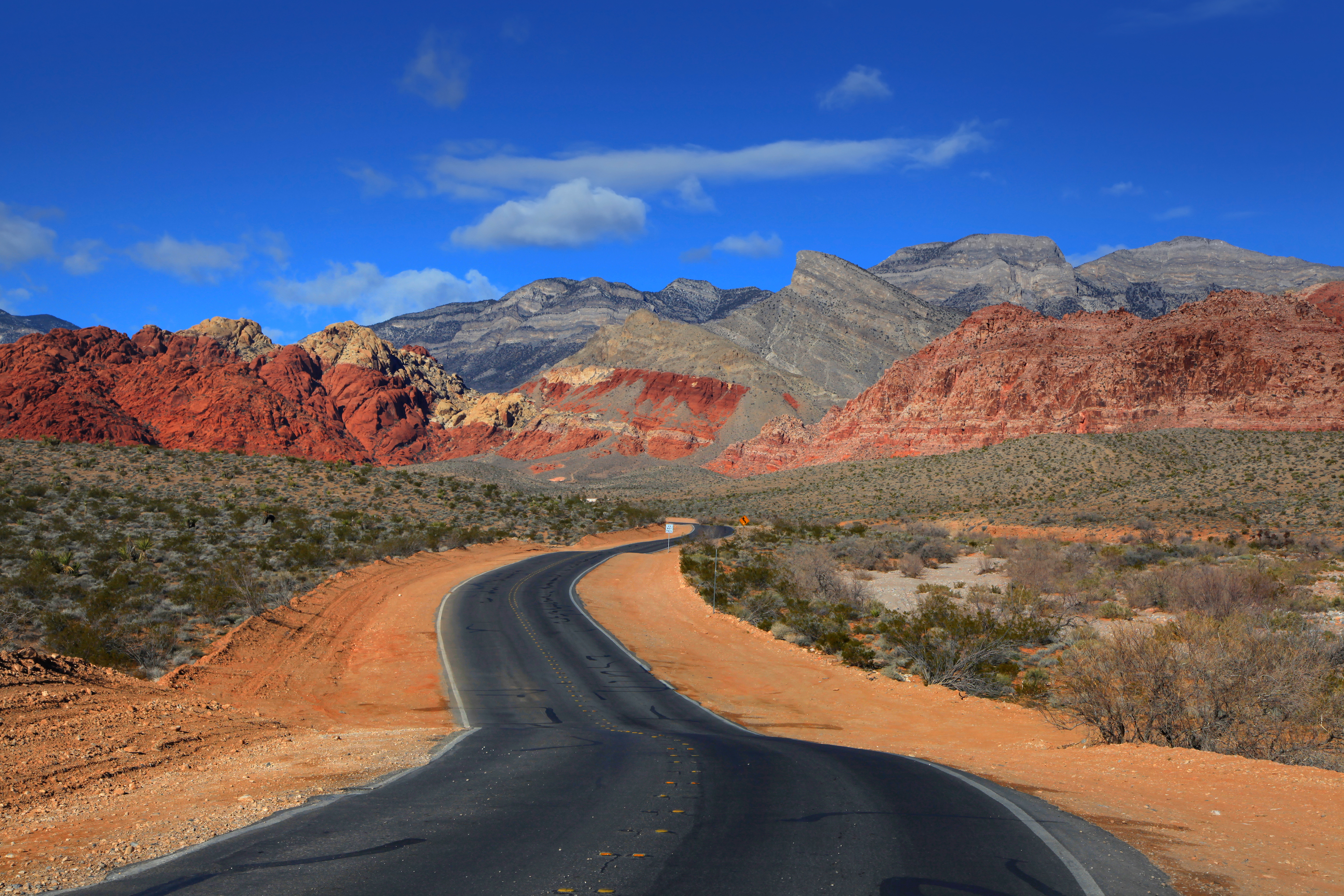 A road running through a desert landscape up to red rocky mountains.