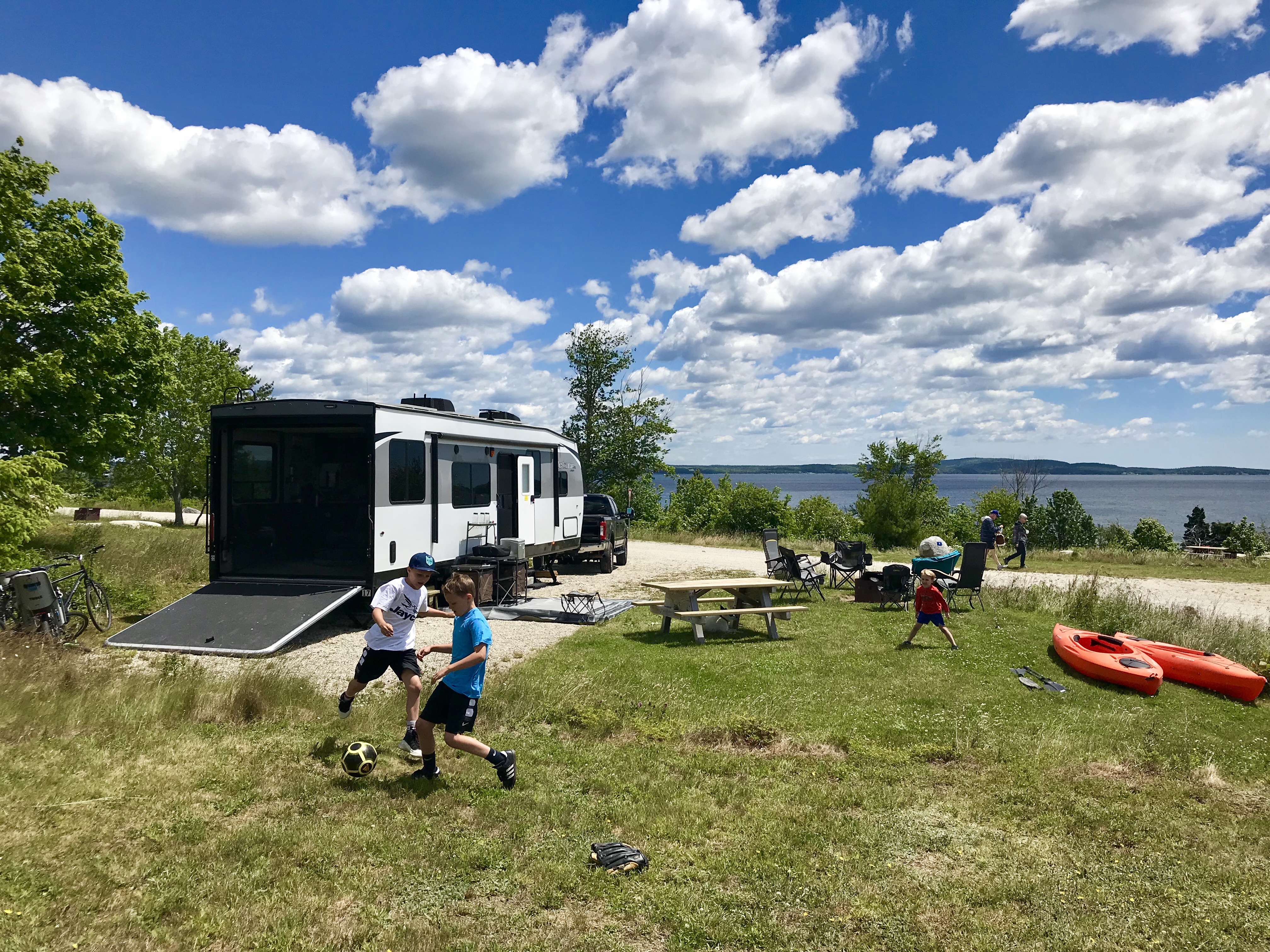 Boys play in the grass on a beautiful, sunny day with the Toy Hauler parked at the edge of a lake. 